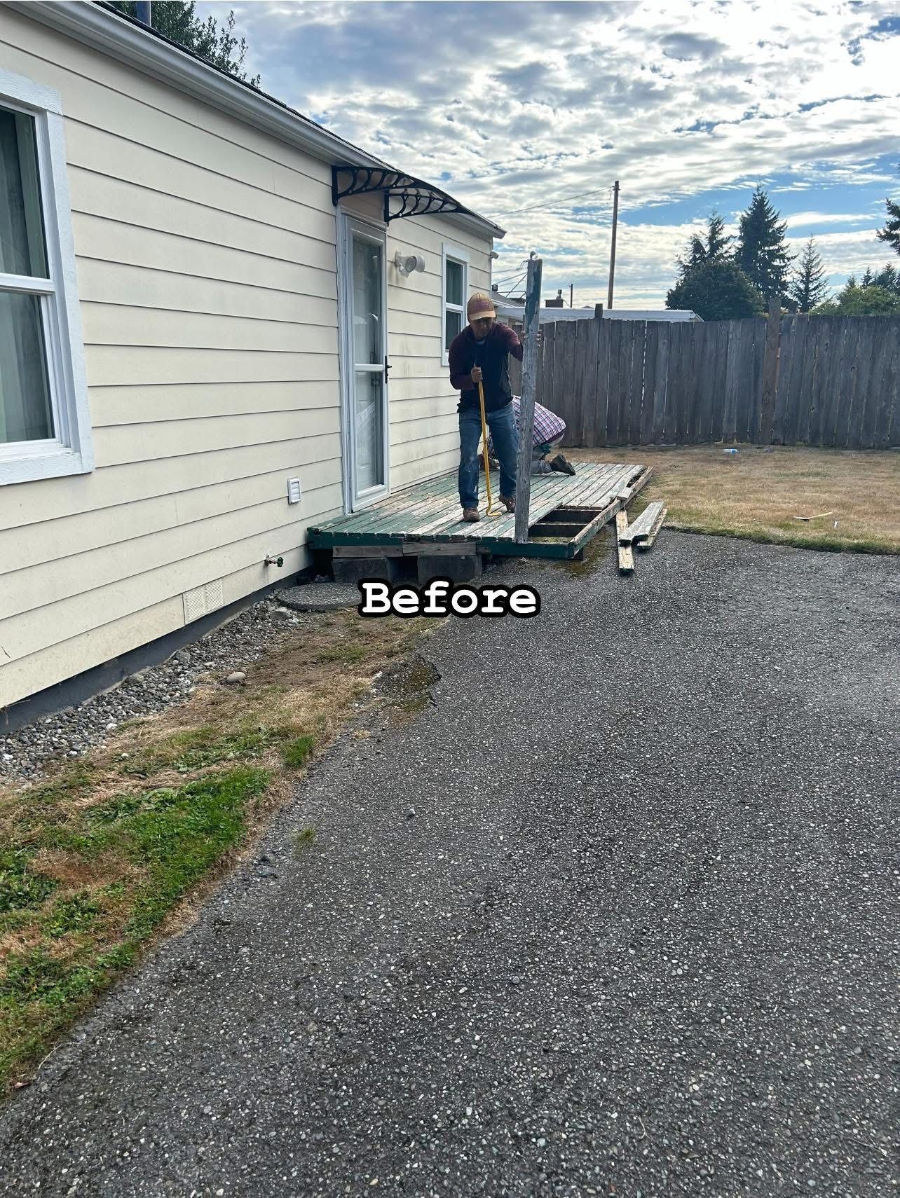 Man on a weathered porch next to a house with gravel driveway and overgrown grass.