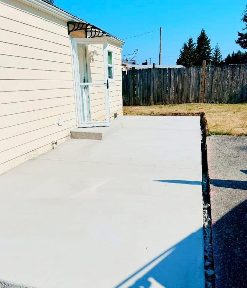 Newly poured concrete patio next to a house with a door, fence, and blue sky.