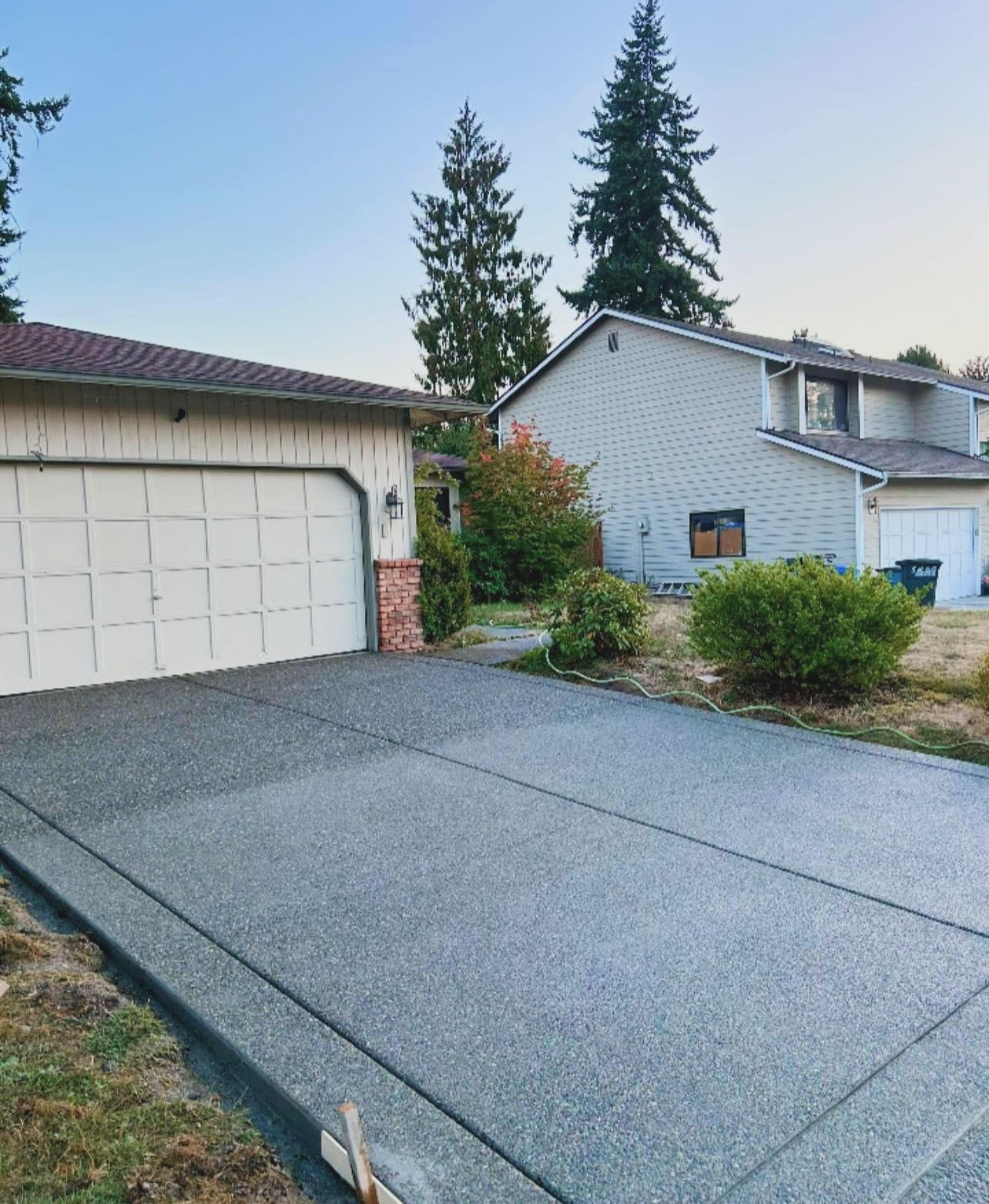 Driveway in front of a house, newly paved, with a garage on the left and a two-story house in the background.