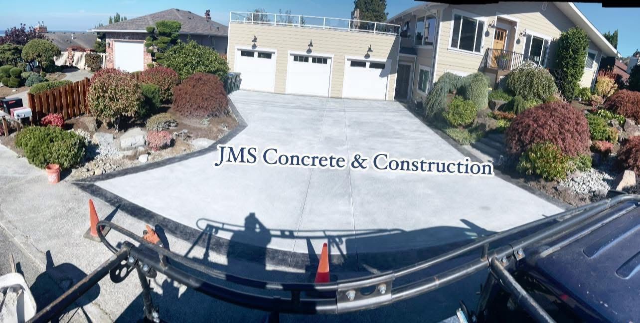 Newly poured concrete driveway in front of a house, with garage doors and landscaping.