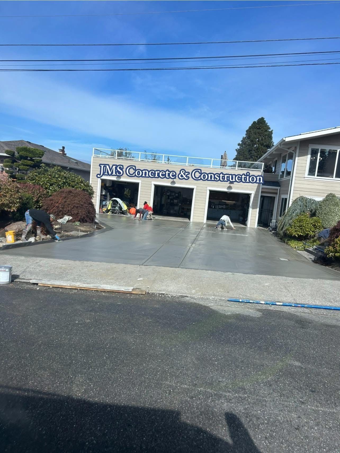 Workers applying sealant to a newly poured concrete driveway