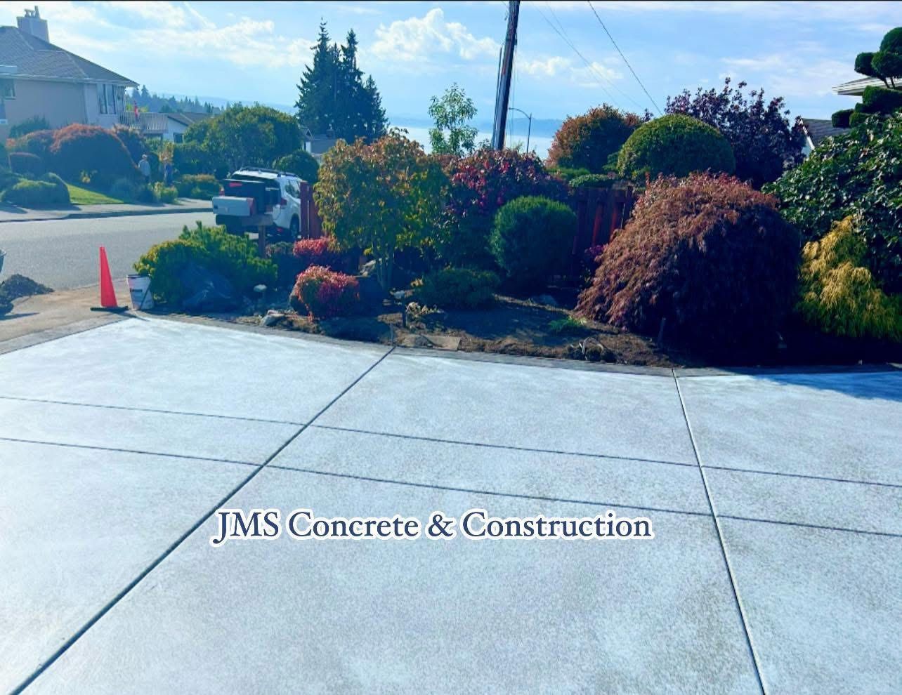 Concrete driveway with landscaping and a distant body of water.