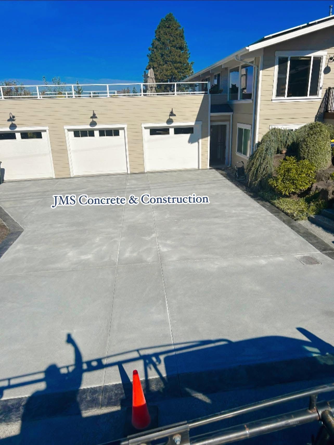 Gray concrete driveway in front of a house with three white garage doors.