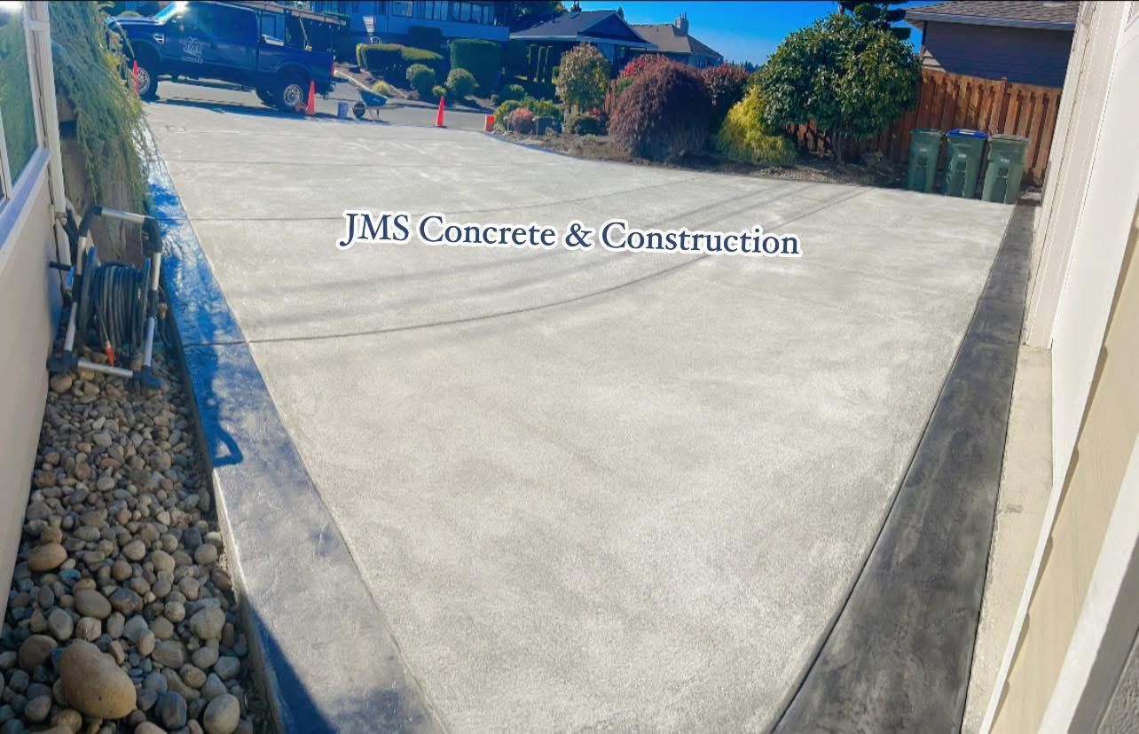 Newly poured concrete driveway with JMS Concrete & Construction logo; gray and black borders.