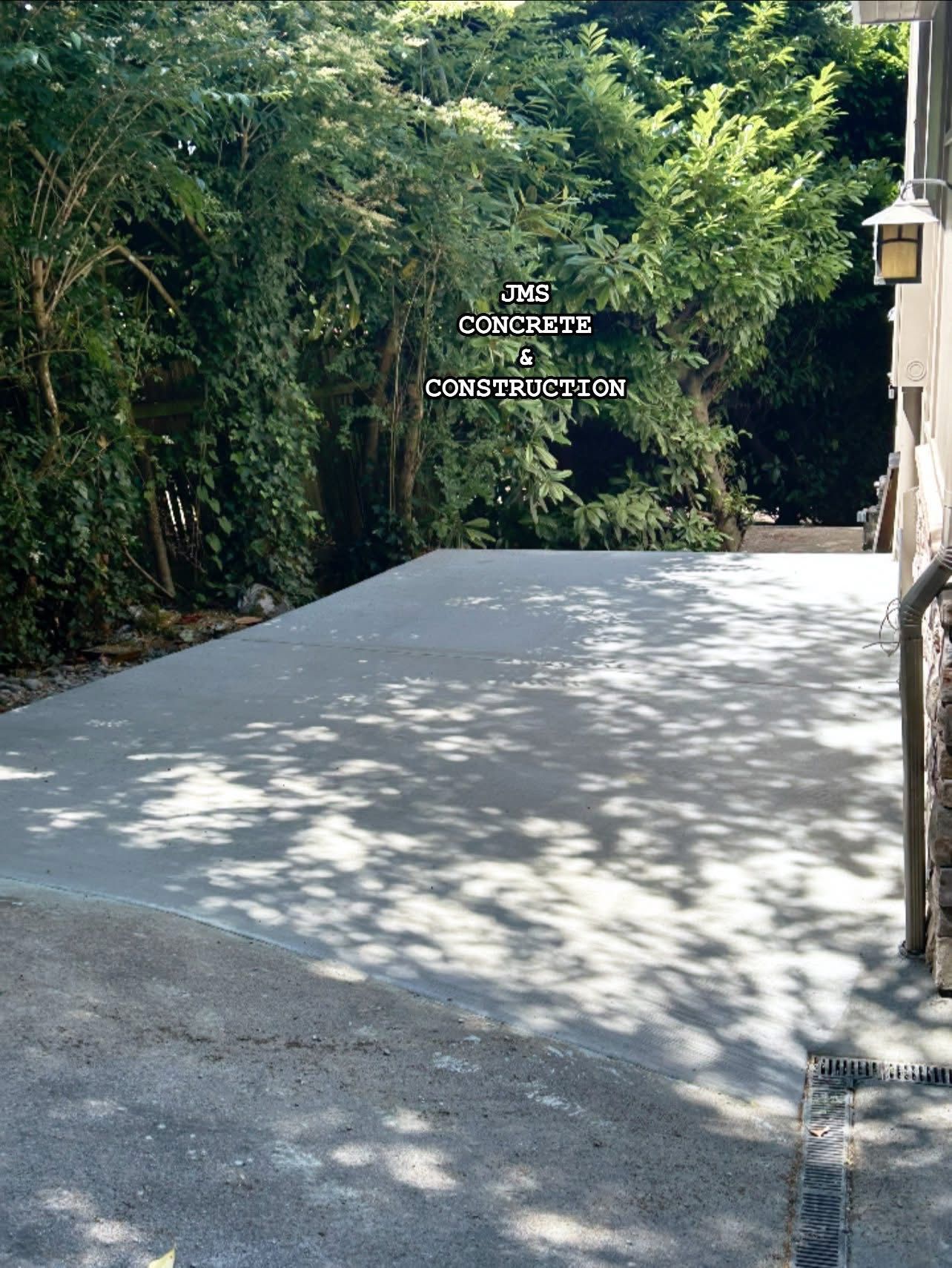 Newly poured concrete patio next to a building, dappled with tree shadows, backed by trees.