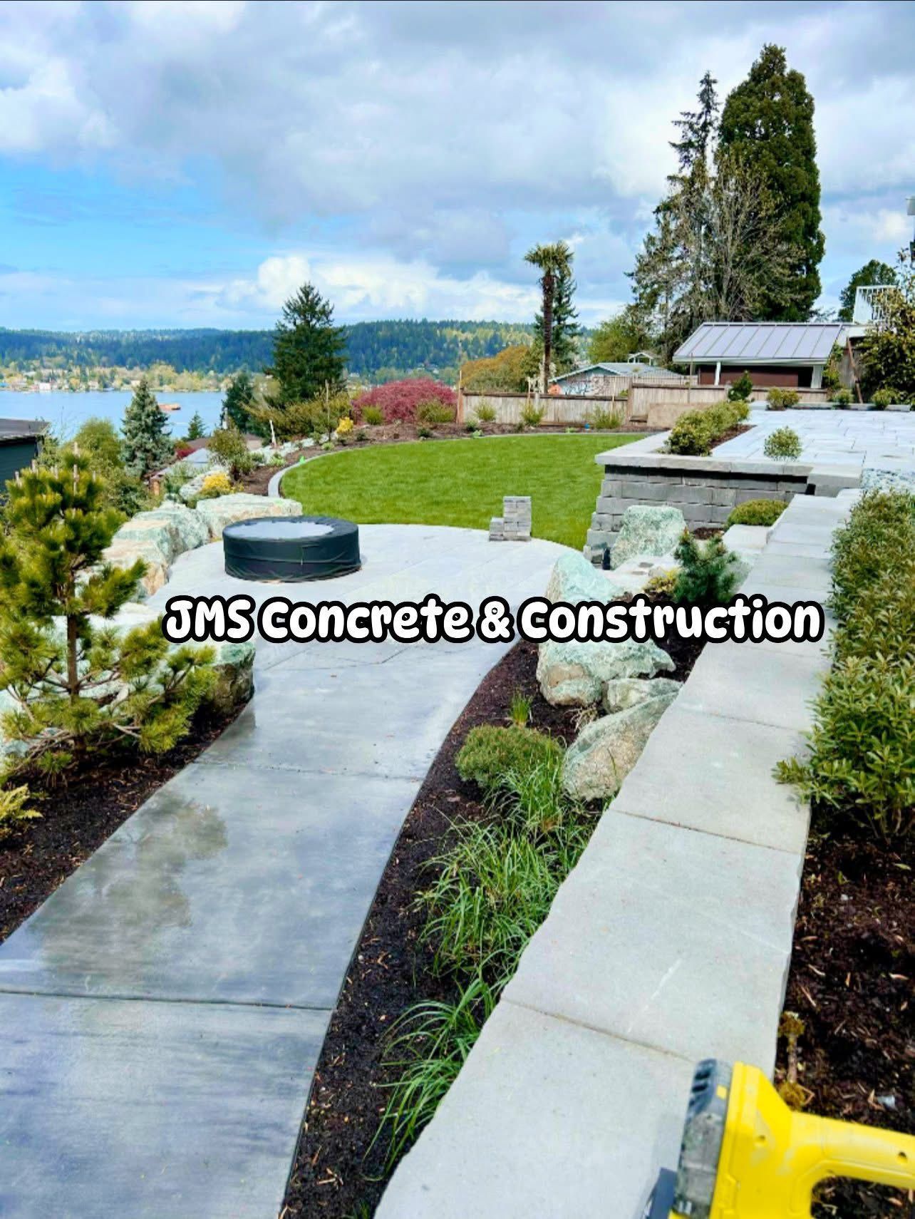 Concrete patio and walkway with a view of a lake and landscaping. JMS Concrete & Construction logo is visible.
