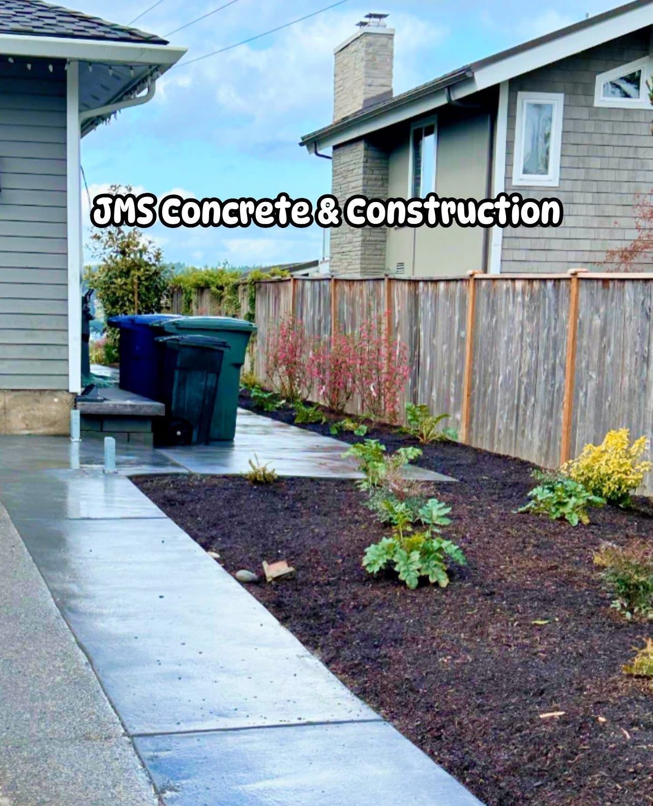 Concrete walkway and garden bed next to a wooden fence and a house; text says