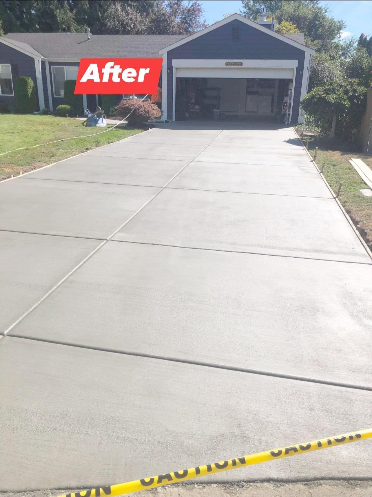 Newly poured concrete driveway in front of a blue house with attached garage;