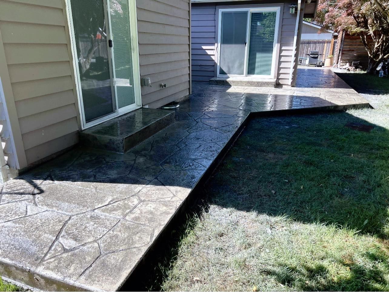 Gray concrete patio next to house with two sliding glass doors and lawn.