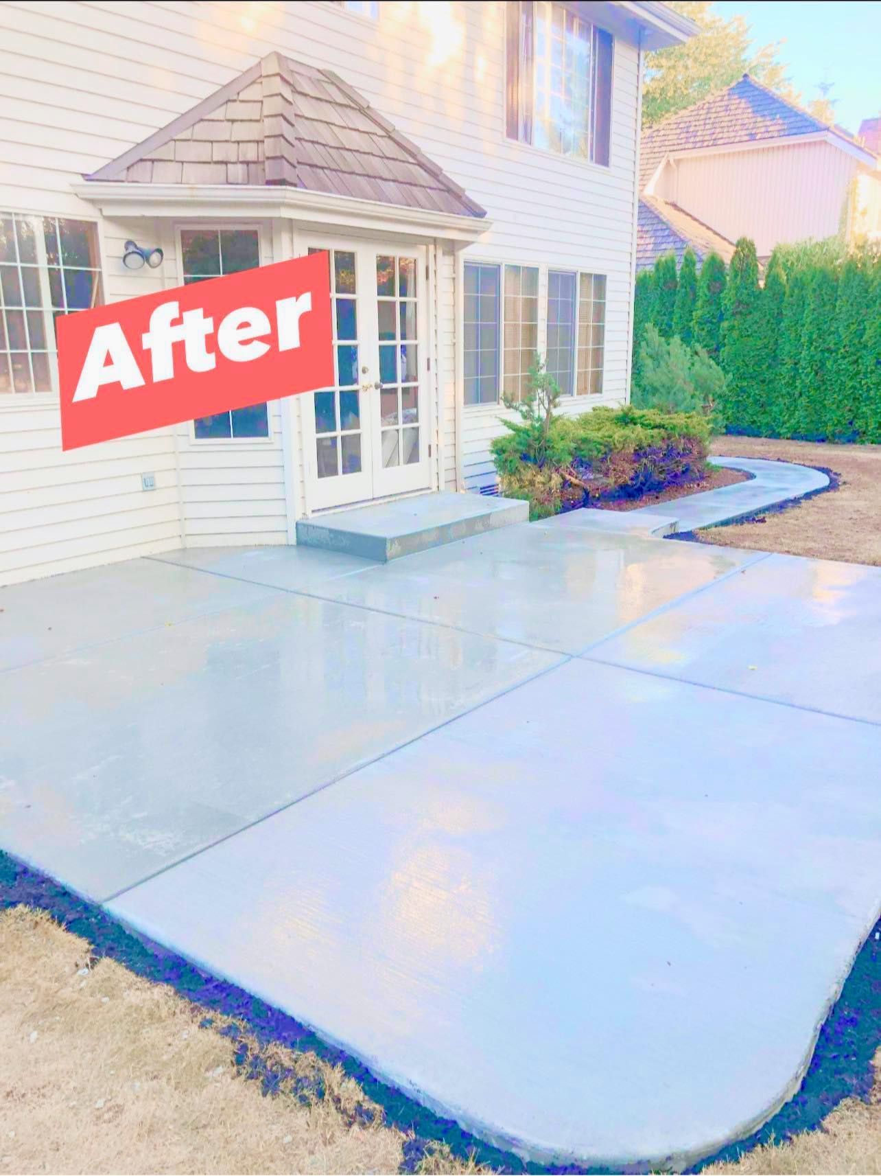 Newly poured concrete patio outside a two-story house with a small garden area.