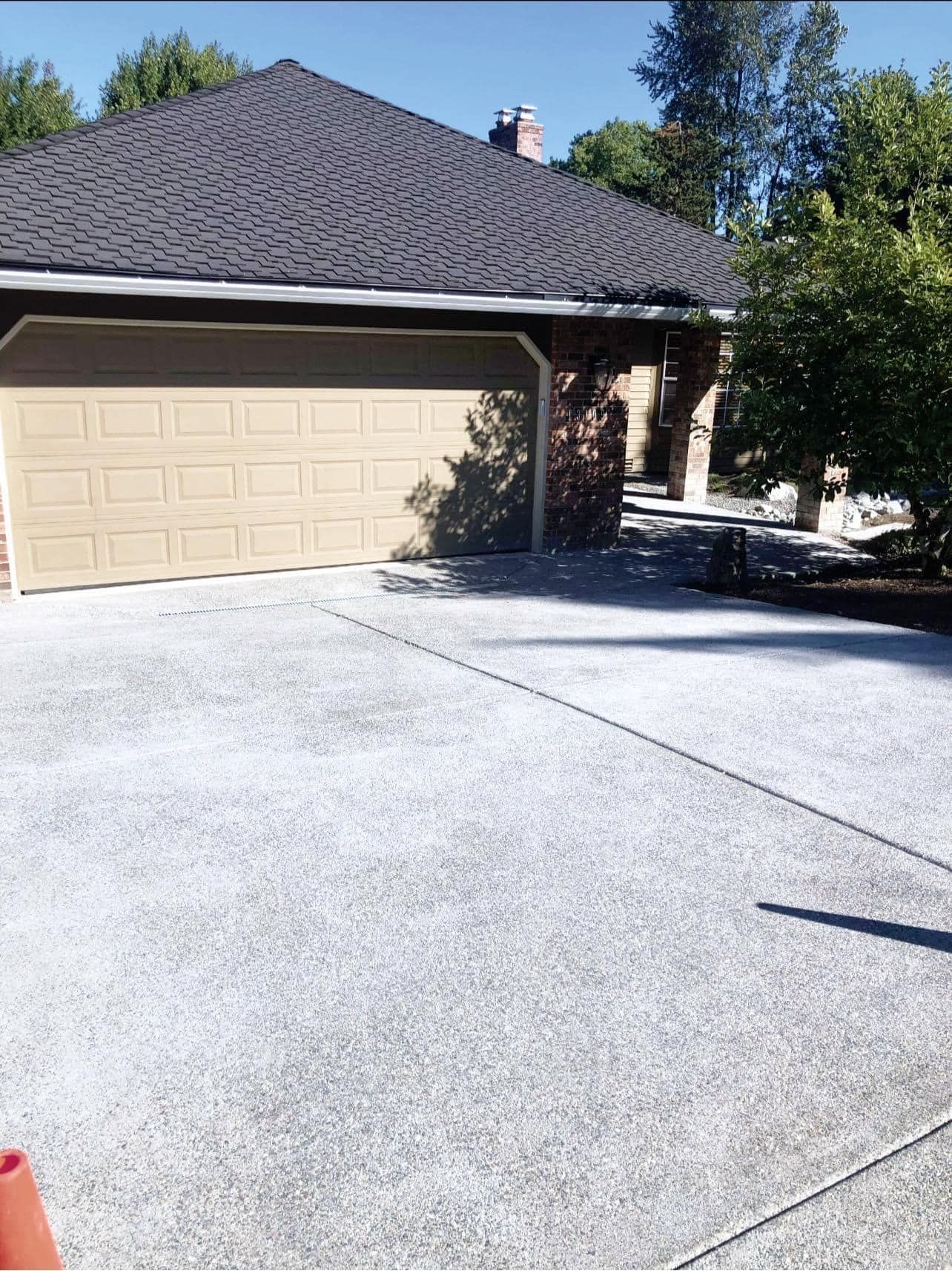 Driveway leading to a garage under a brown-shingled roof. A brick house is in the background.