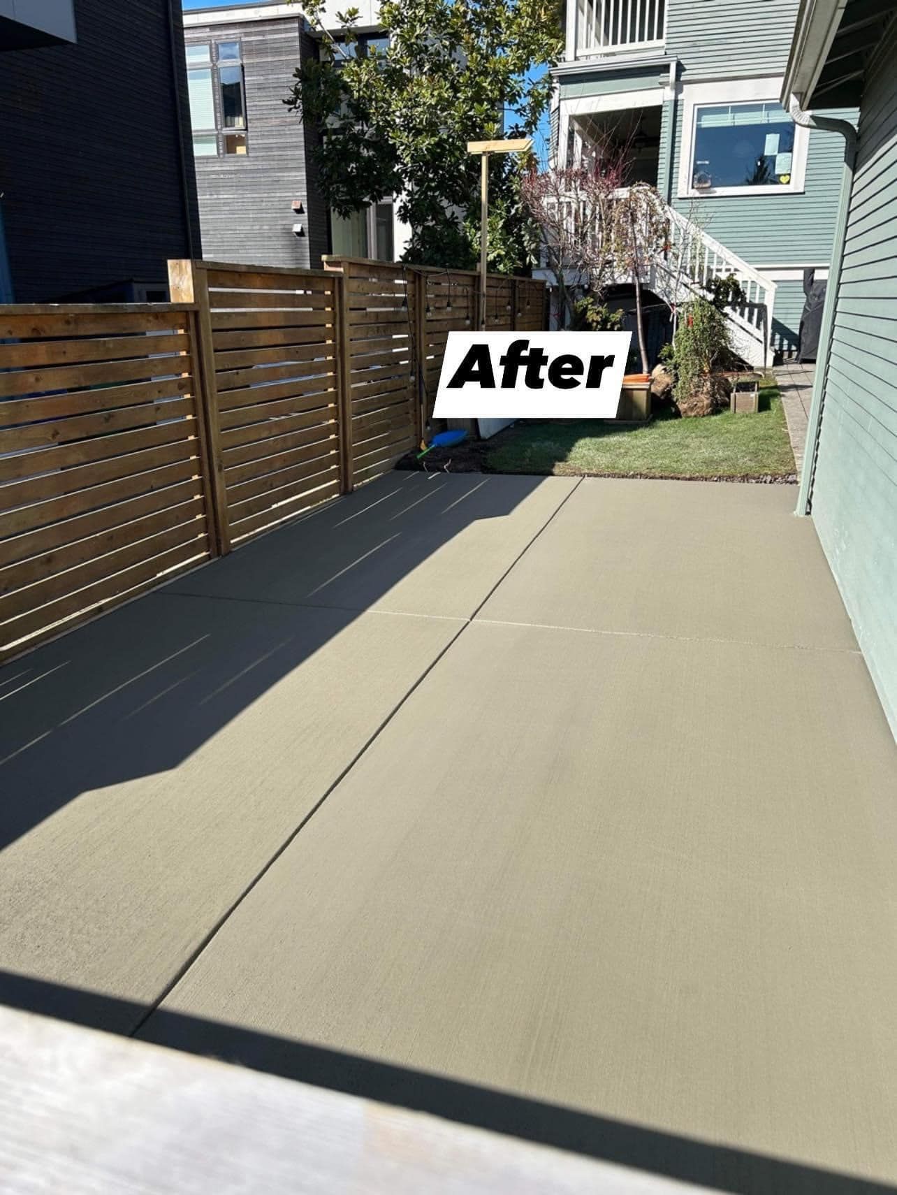 Newly poured concrete patio next to a wooden fence and house.