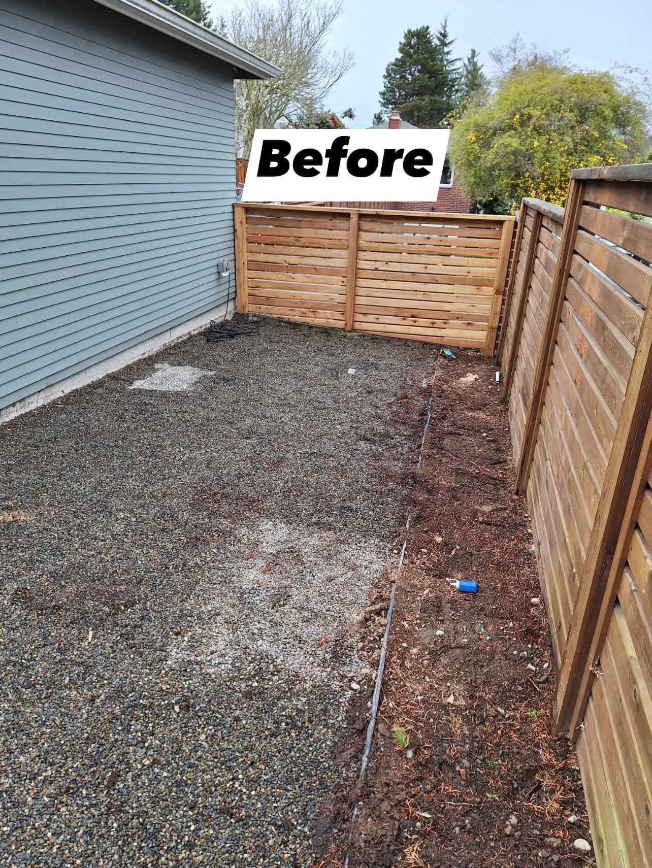 Gravel and mulch yard next to a light blue building and wooden fences labeled 