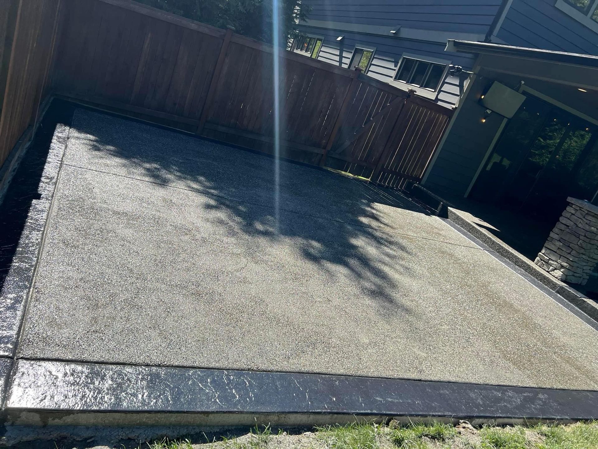 Gravel patio with dark border and wood fence. Sunny outdoor setting.