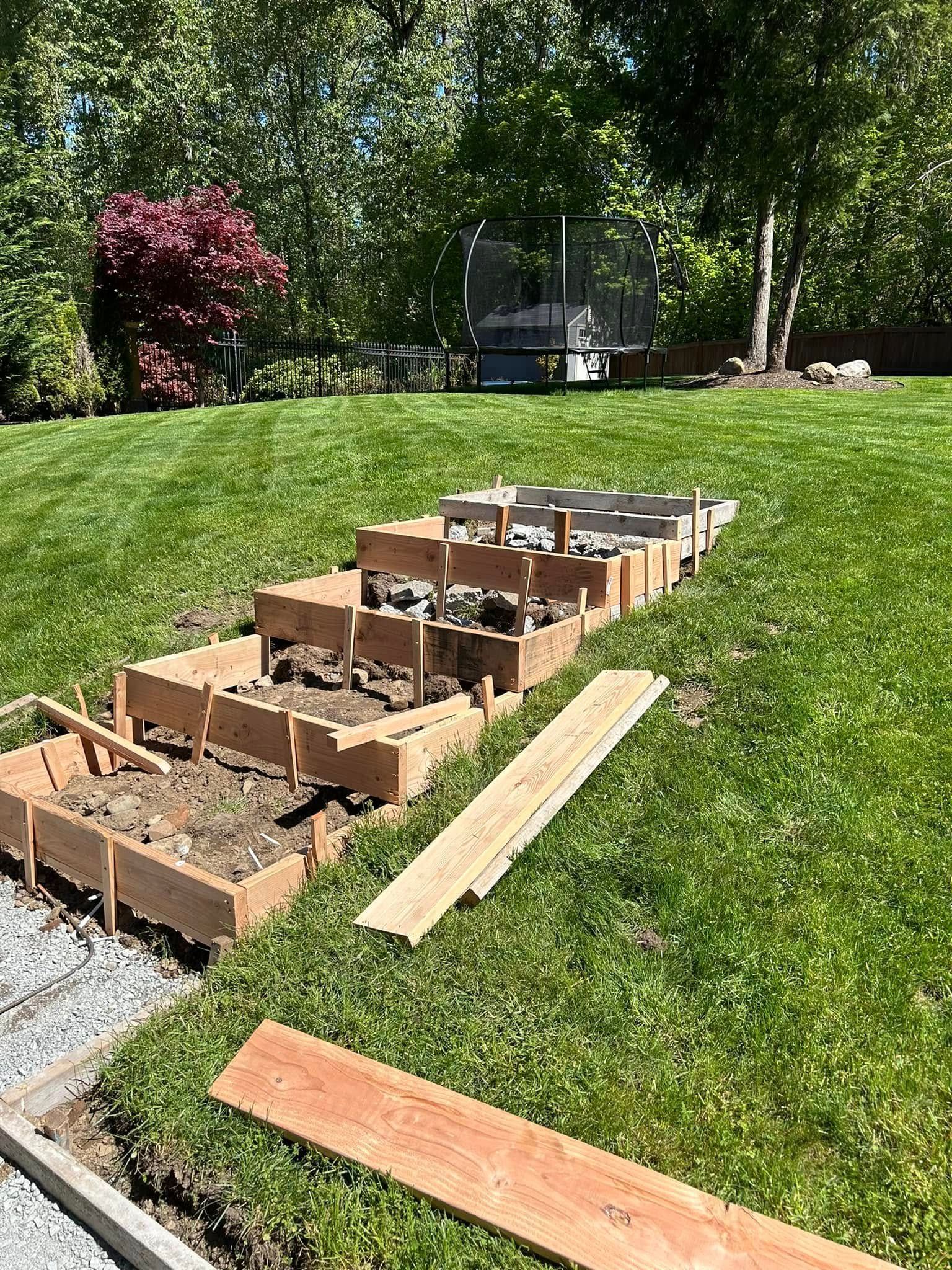 Raised garden beds under construction on a grassy lawn; wooden frames are visible.