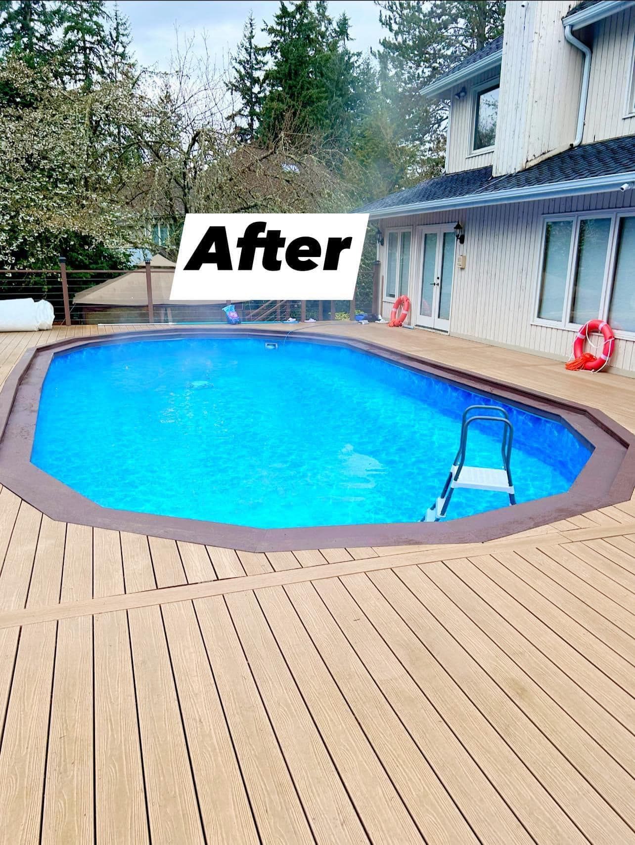 An oval-shaped swimming pool surrounded by a wooden deck, next to a two-story house.