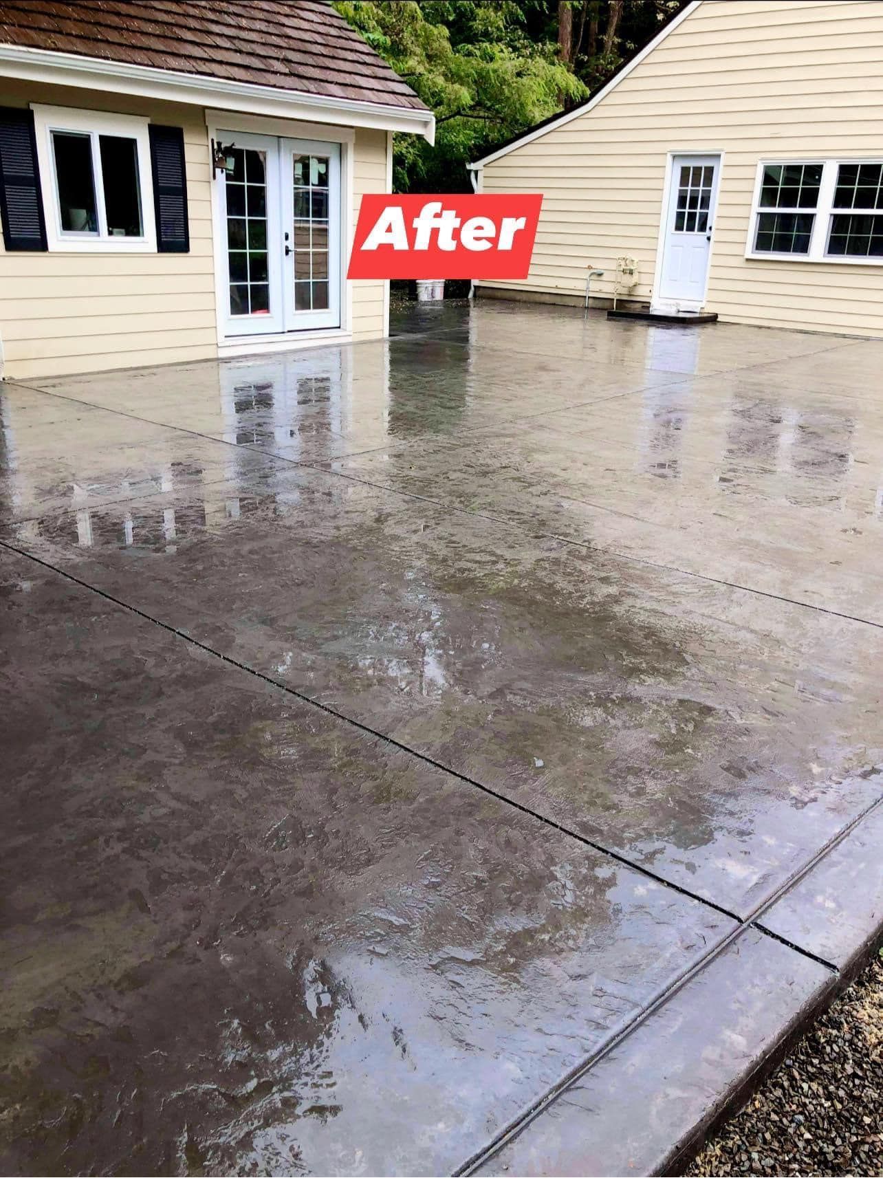 Newly poured, dark gray concrete patio in front of a tan house and garage.