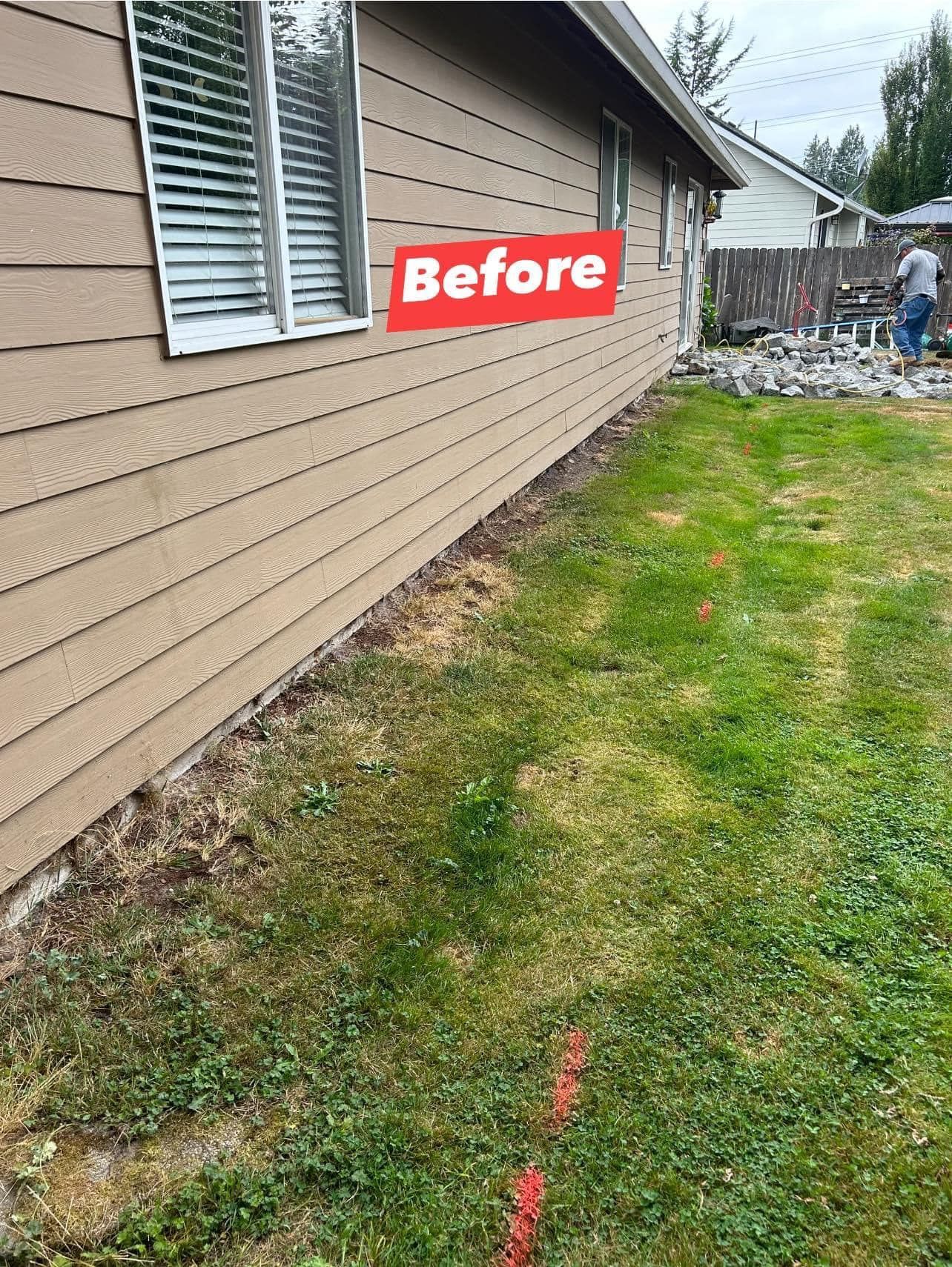 Exterior of a house before landscaping. Brown siding, green lawn, and a person in the background.