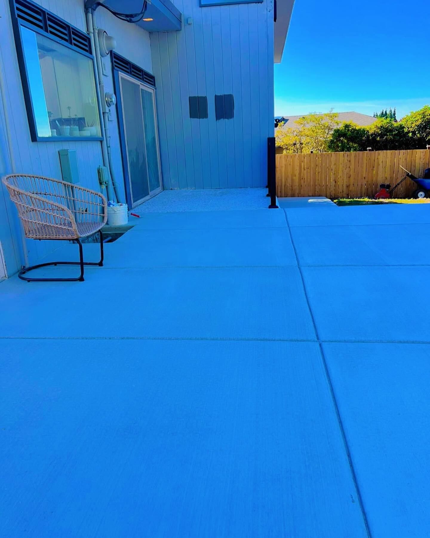 Blue concrete patio next to a house with a chair and sliding glass doors. A wooden fence is in the background.