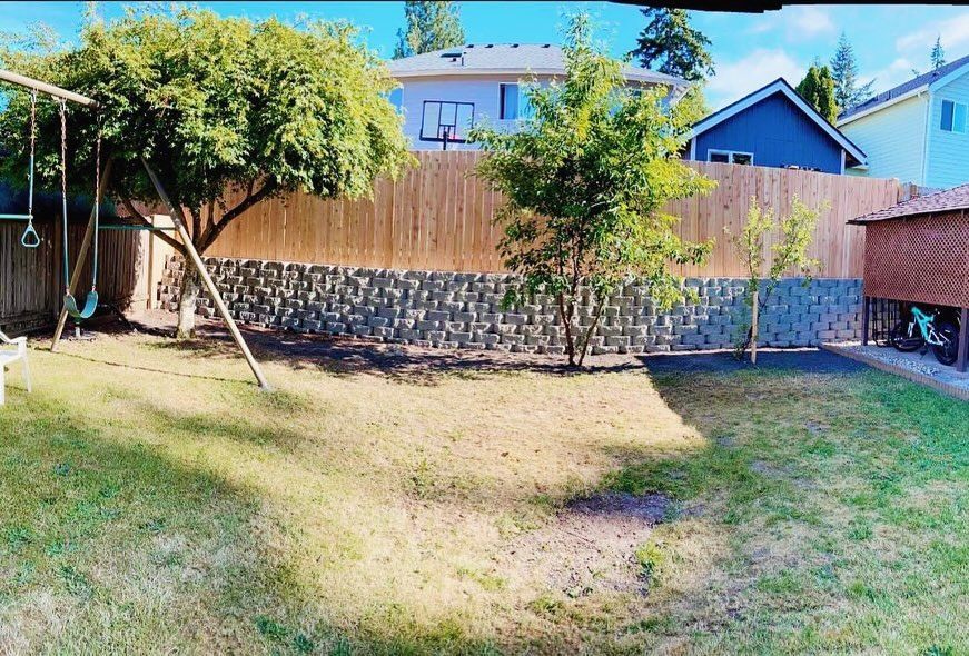 Backyard with grass, swing set, trees, and a wooden fence.