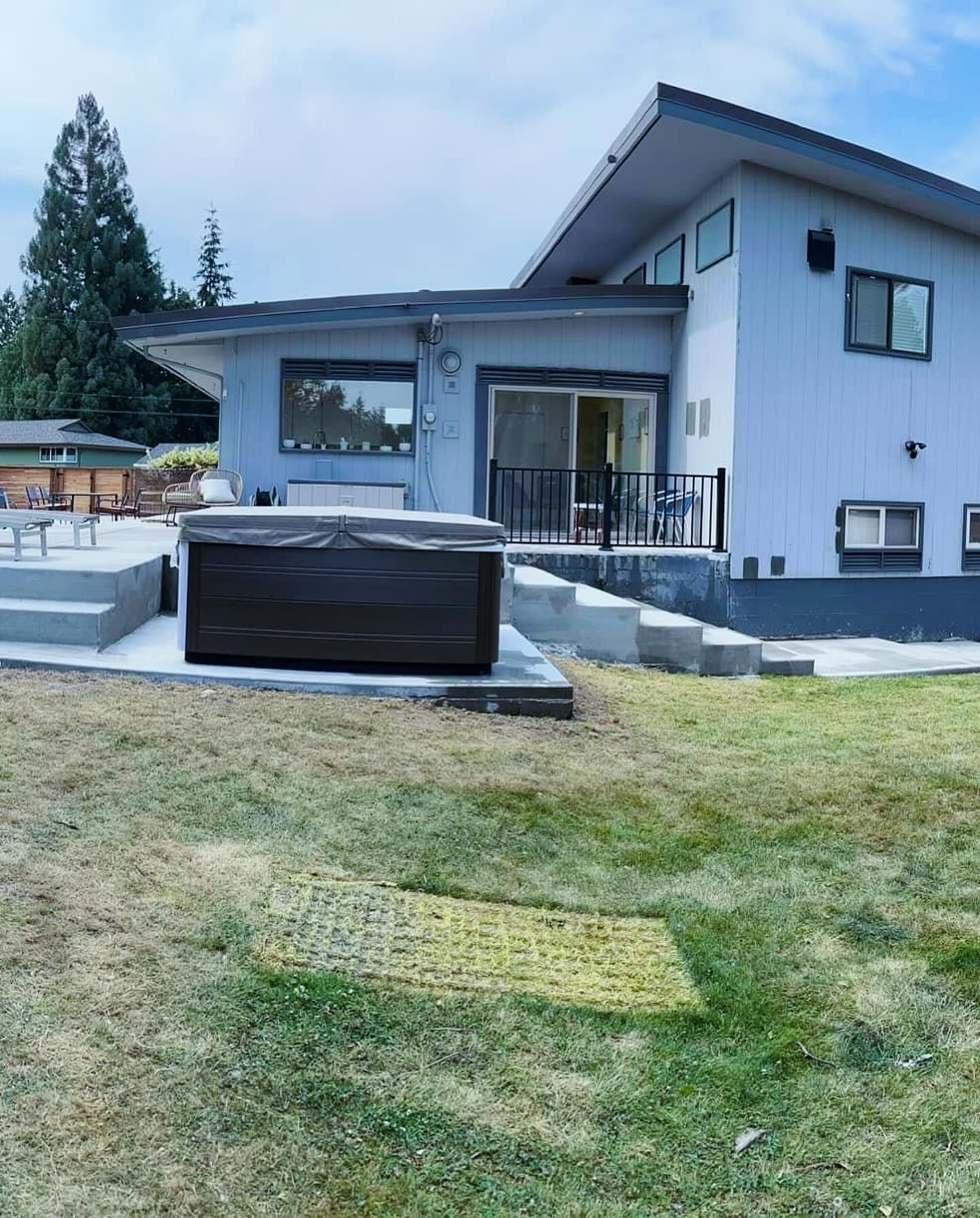 Backyard with a light blue two-story house, a hot tub, and a grassy lawn.