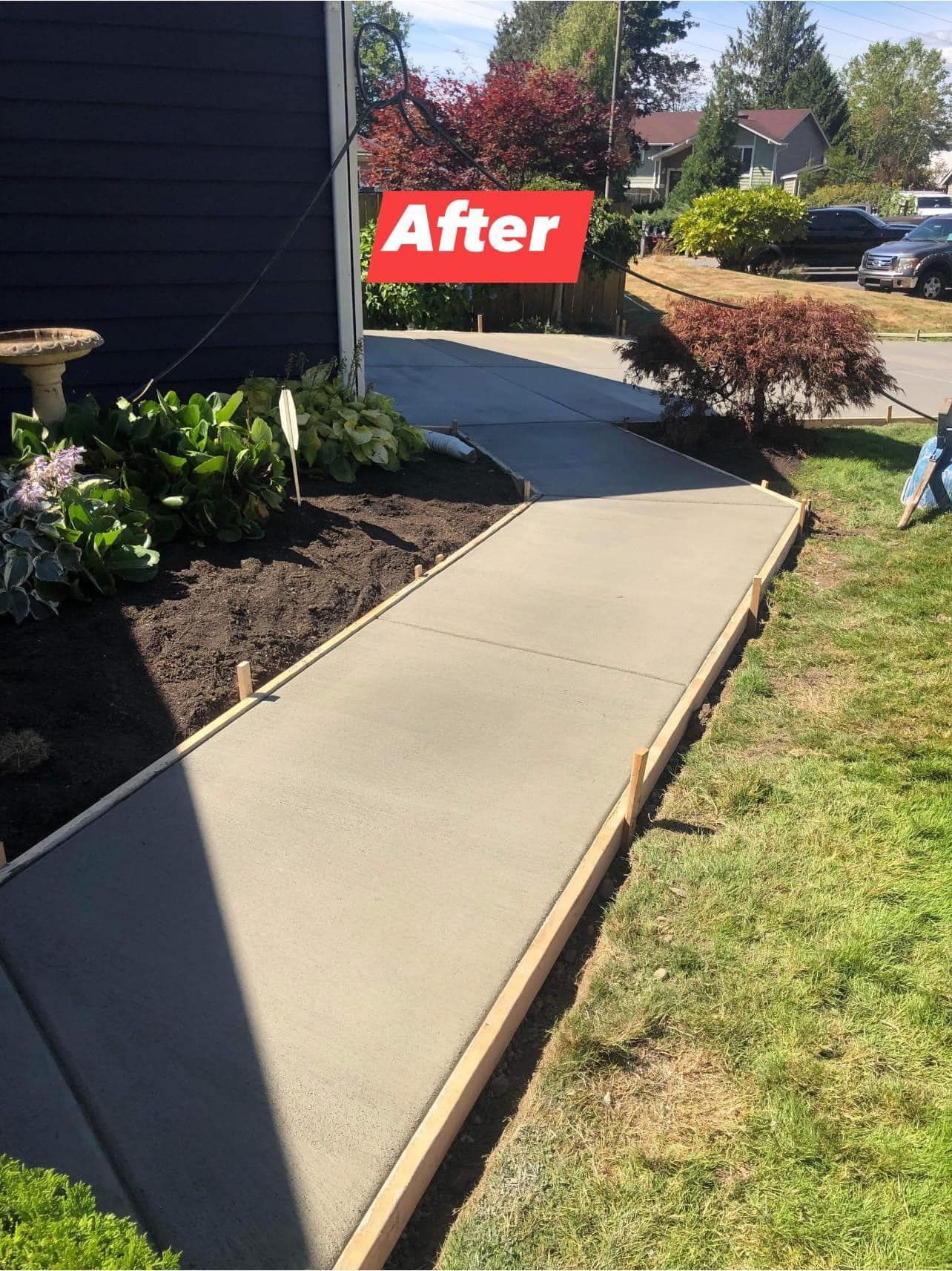 Freshly poured concrete sidewalk, framed by wooden boards, with a red