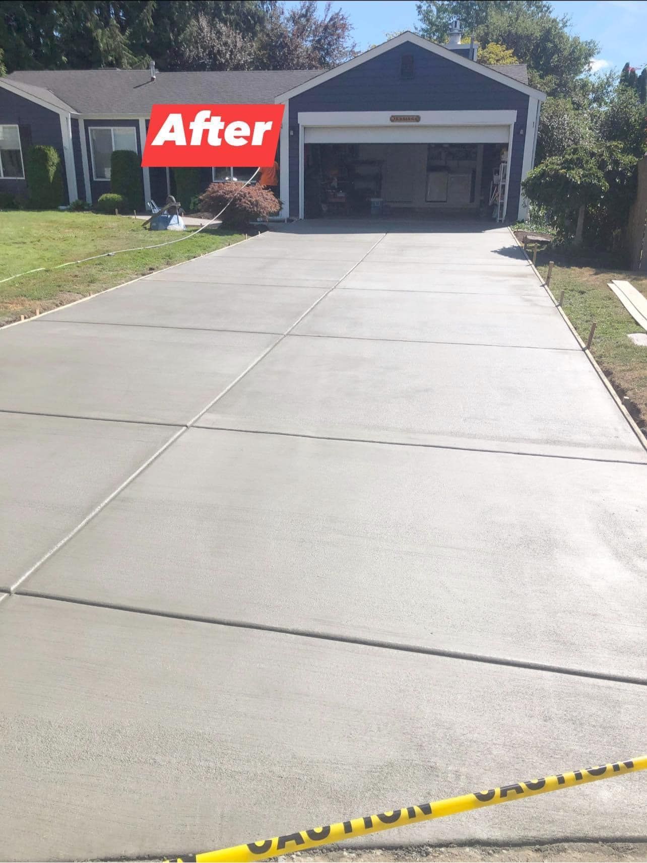 Newly poured gray concrete driveway in front of a blue house, labeled