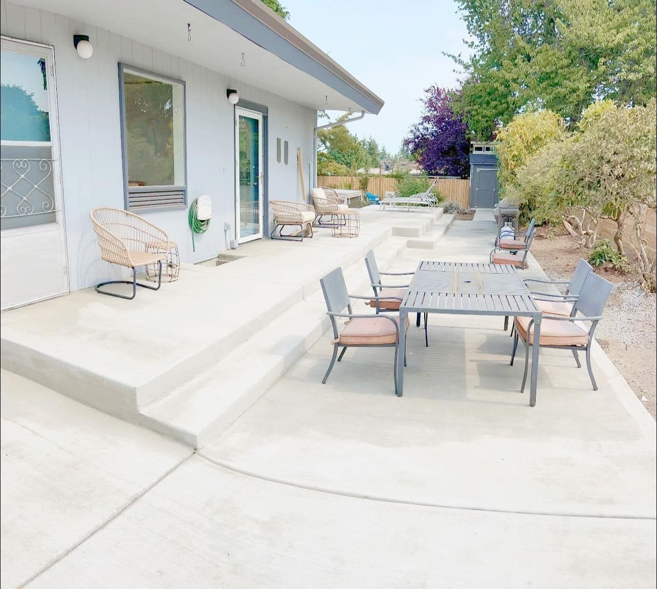 A concrete patio with outdoor furniture; house with large windows; trees in the background.