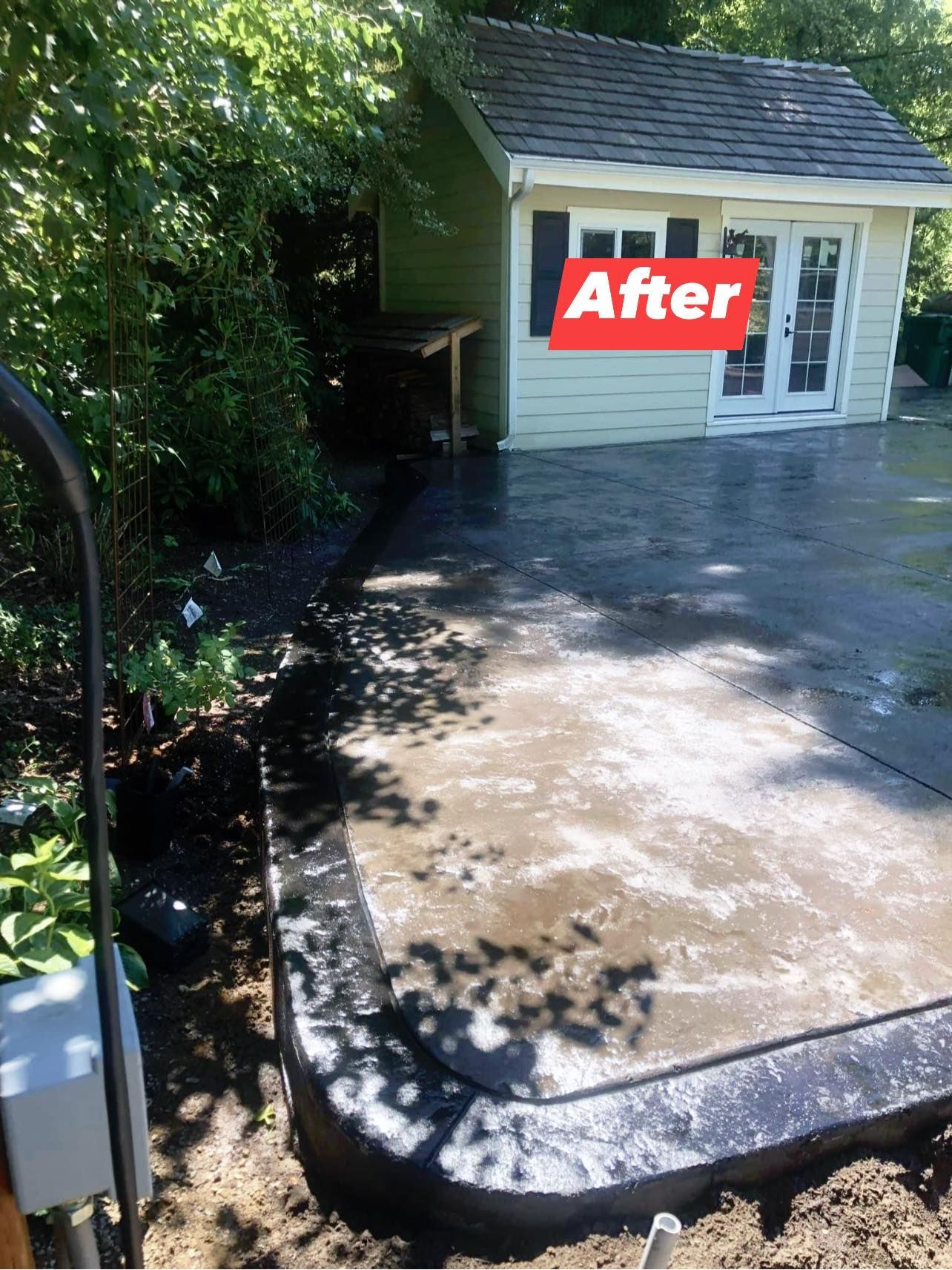 Newly poured concrete patio, with shed in background, surrounded by landscaping.