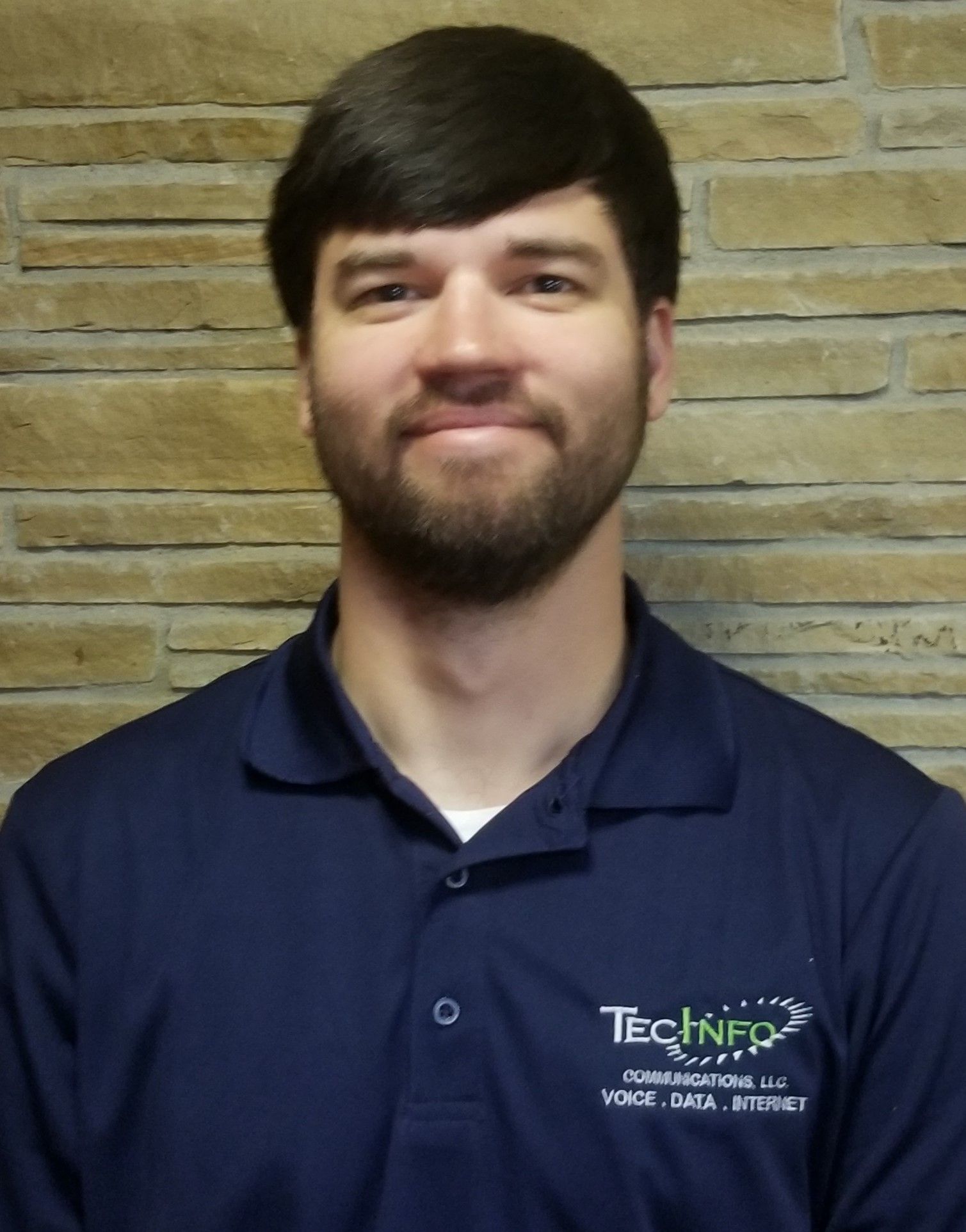 Man in navy polo shirt smiling in front of a tan brick wall