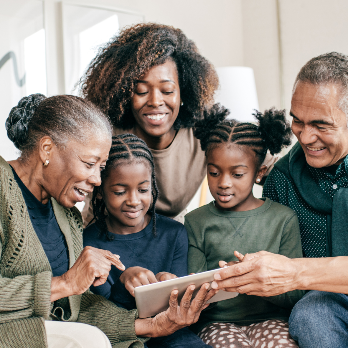 Family gathered on a couch, smiling while sharing a tablet together