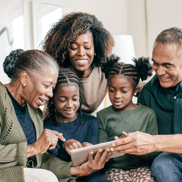 Multigenerational family smiling and using a tablet together on a couch
