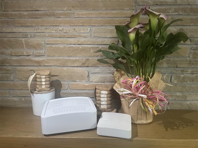White decorative devices on a table beside a potted plant and basket of flowers against a brick wall