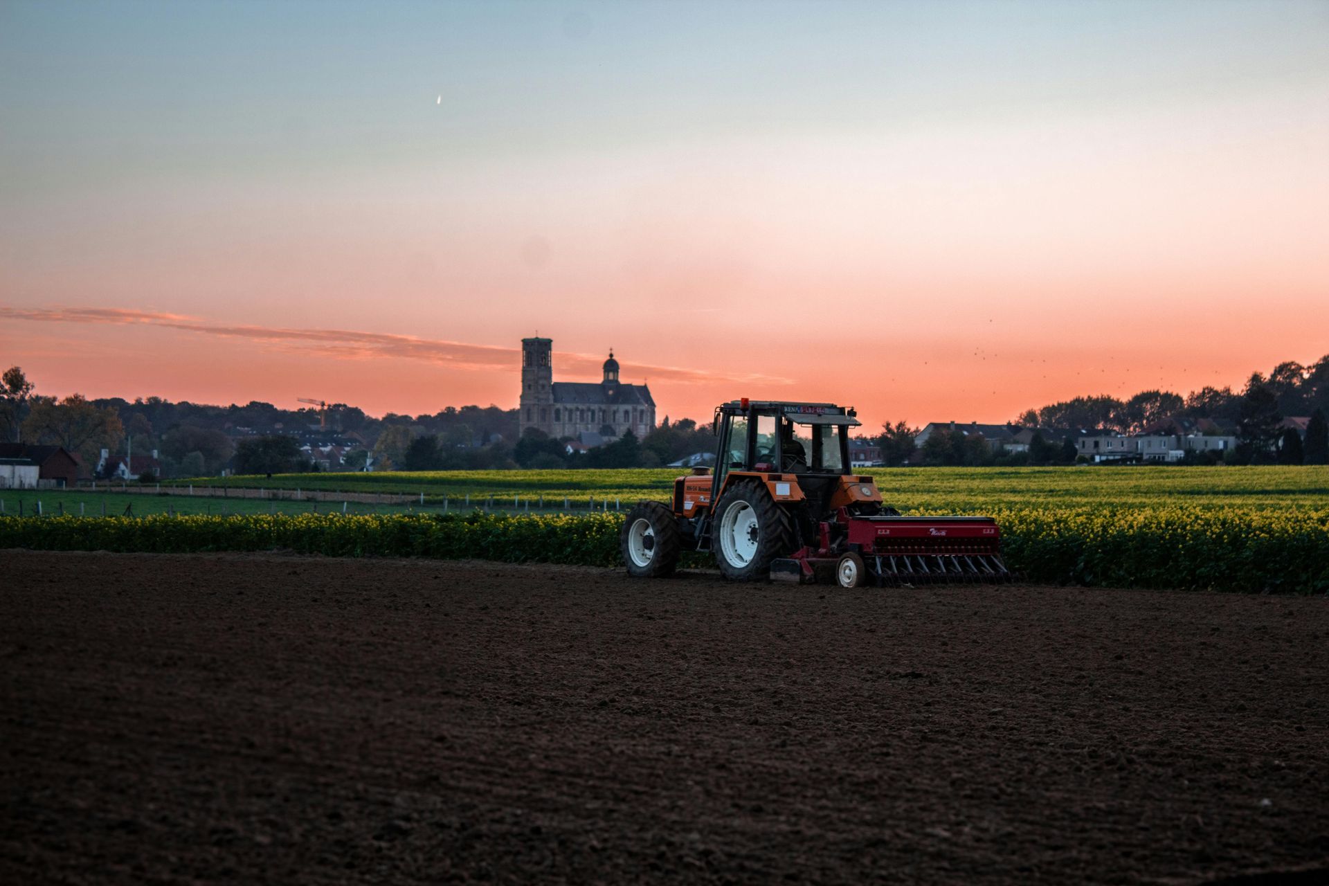 Tractor working a dark field at sunset with a castle silhouette in the distance