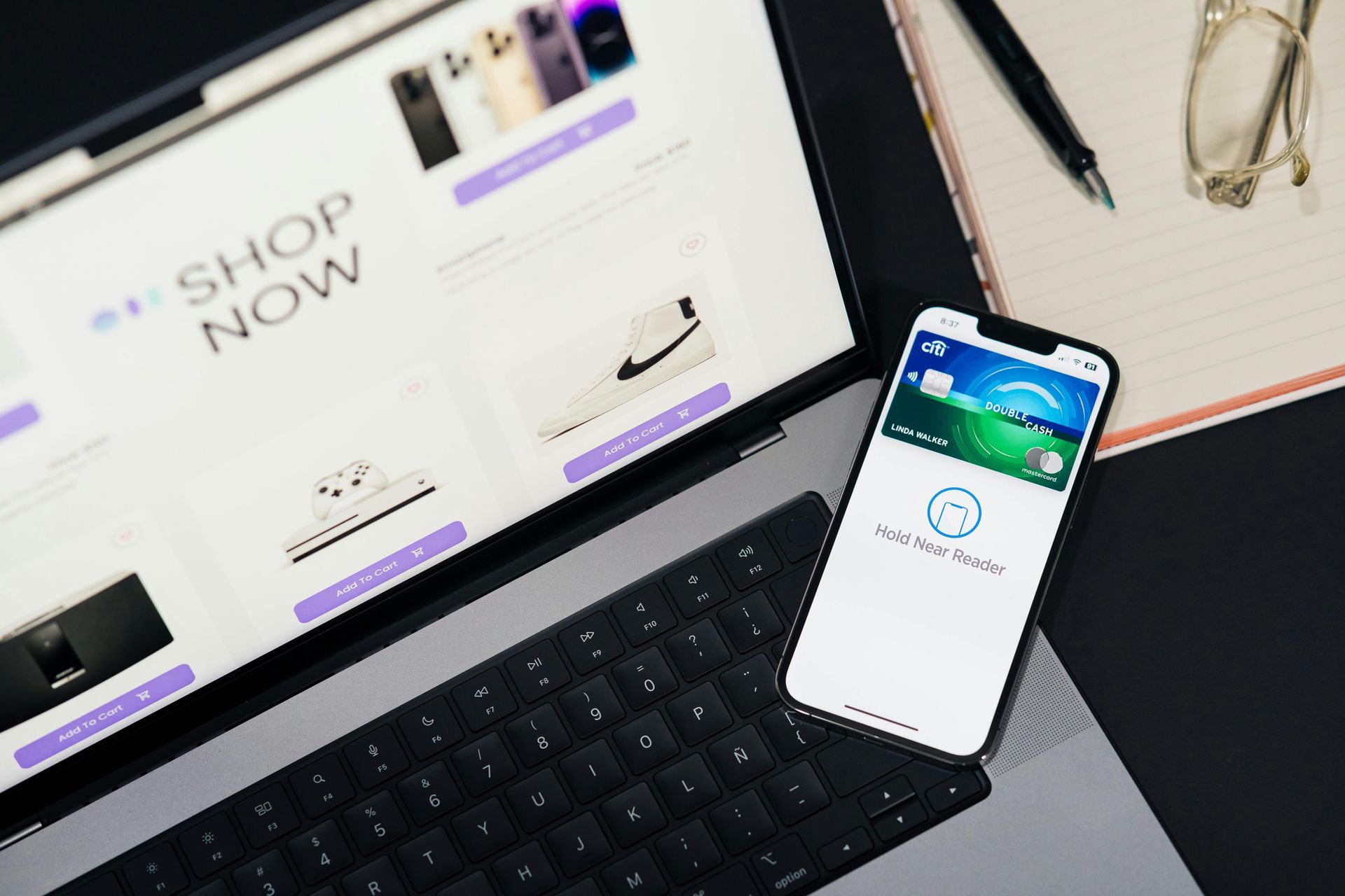 Laptop showing an online shop with a smartphone on the keyboard and eyeglasses nearby