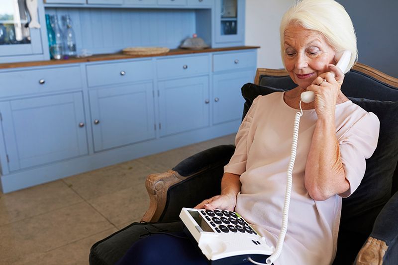 Woman in a light pink sweater using a corded phone while seated in a kitchen chair
