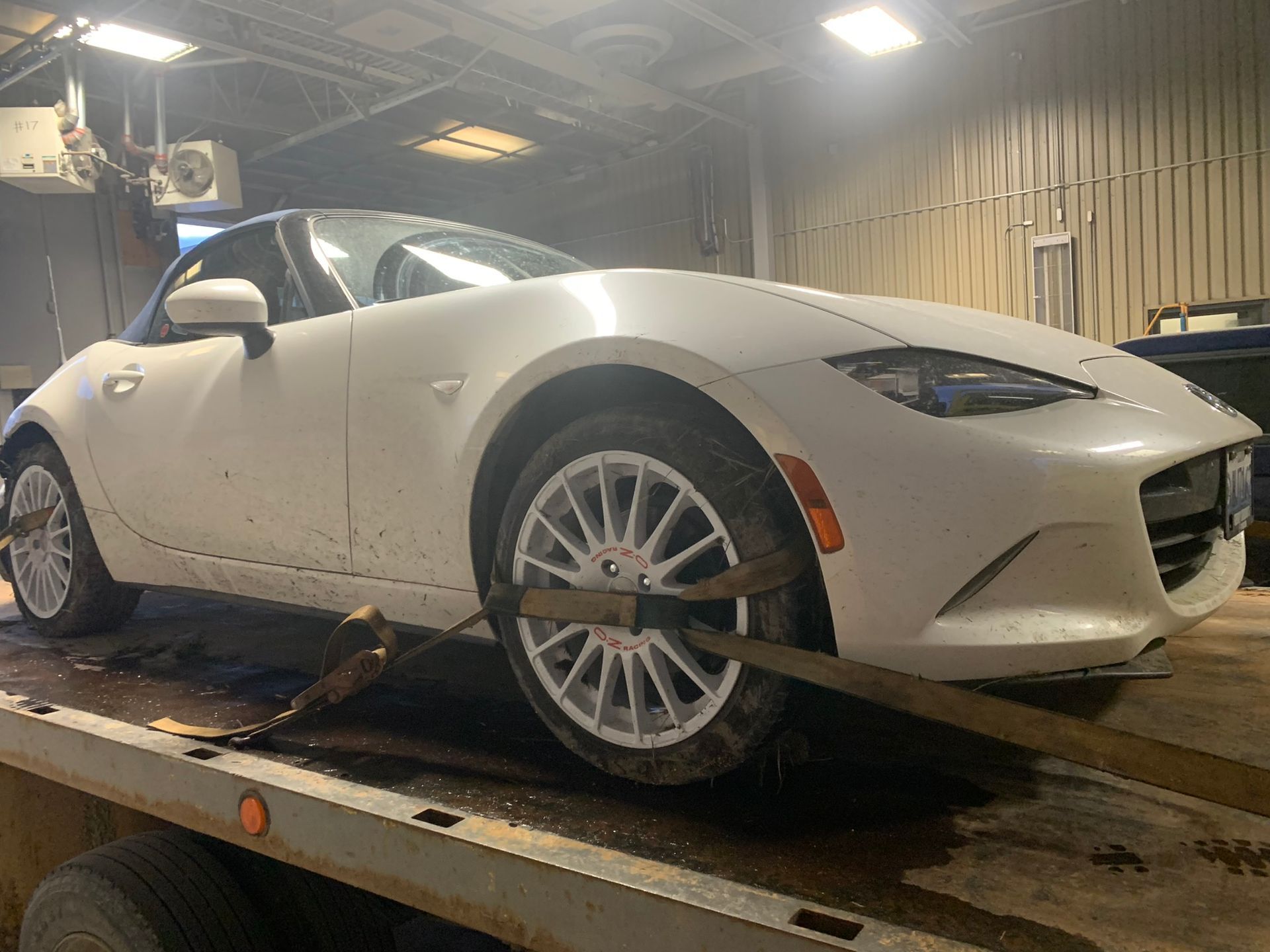 White sports car on a tow truck in a garage, viewed from the front side.