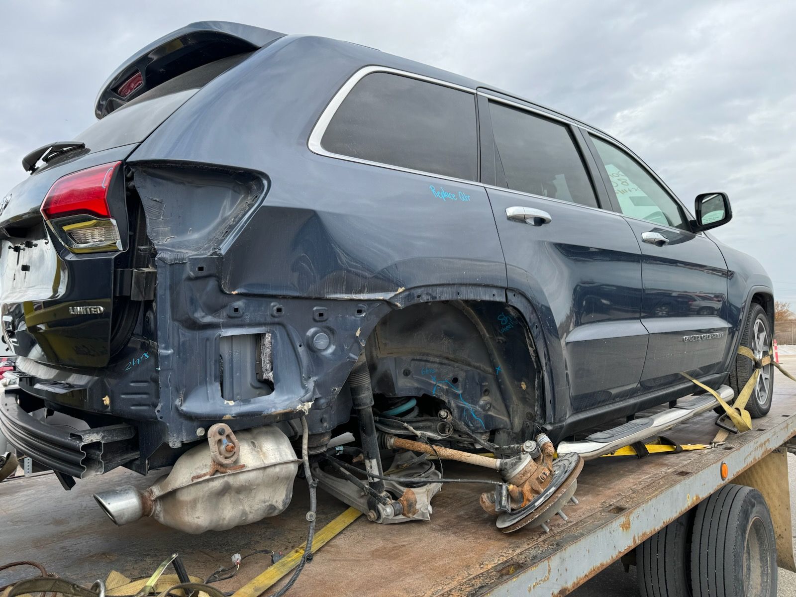Severely damaged dark SUV strapped onto a tow truck, rear and side body crushed.