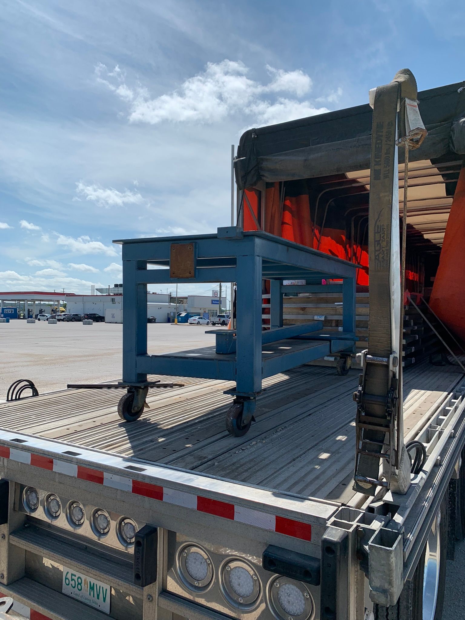 Blue rolling work table on a flatbed truck, with stacked lumber and equipment at a loading dock