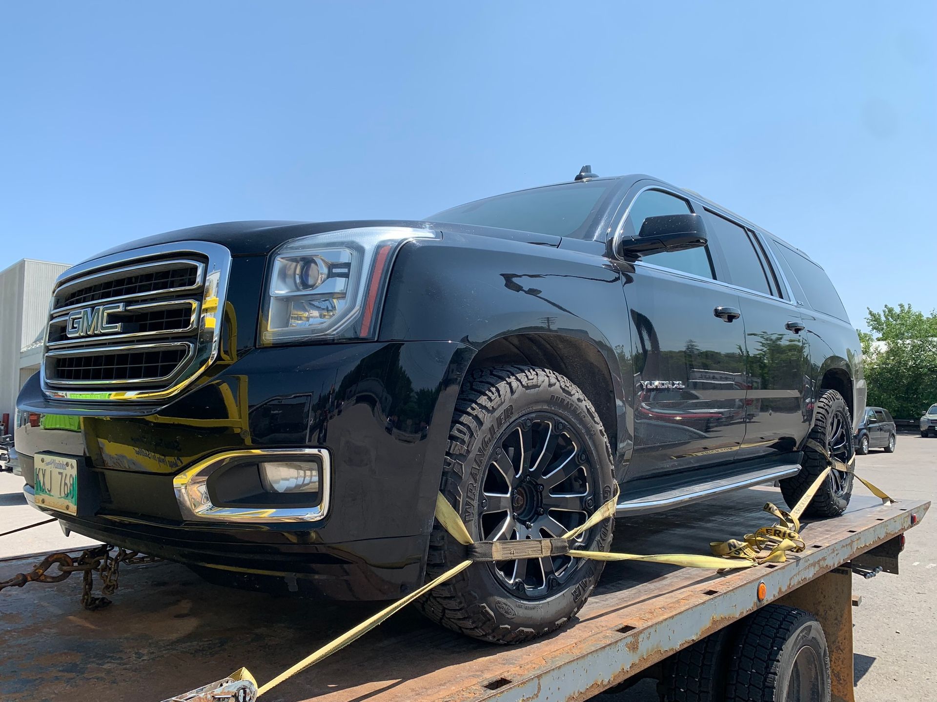 Black GMC SUV strapped on a tow truck bed under a clear blue sky