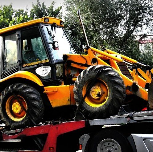 Yellow loader tractor loaded on a red flatbed truck, outdoors among trees.