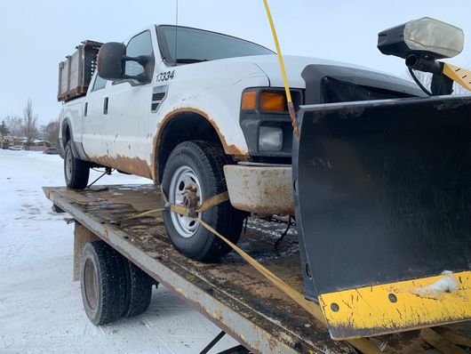 A snowplow is being towed on our flatbed tow truck through the snow.