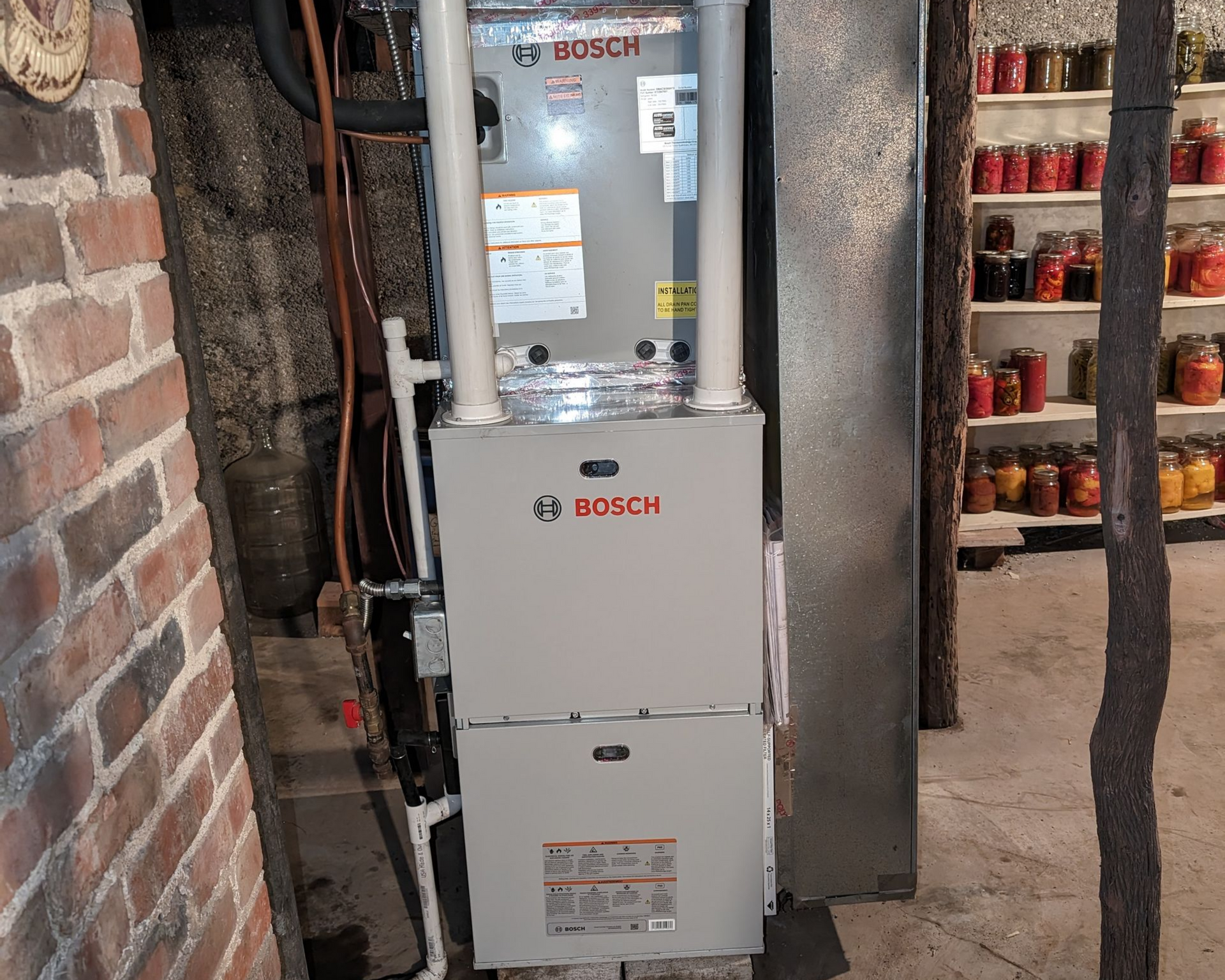 Furnace and water heater in a utility room. Gray appliances with metal vent pipes and gas lines.
