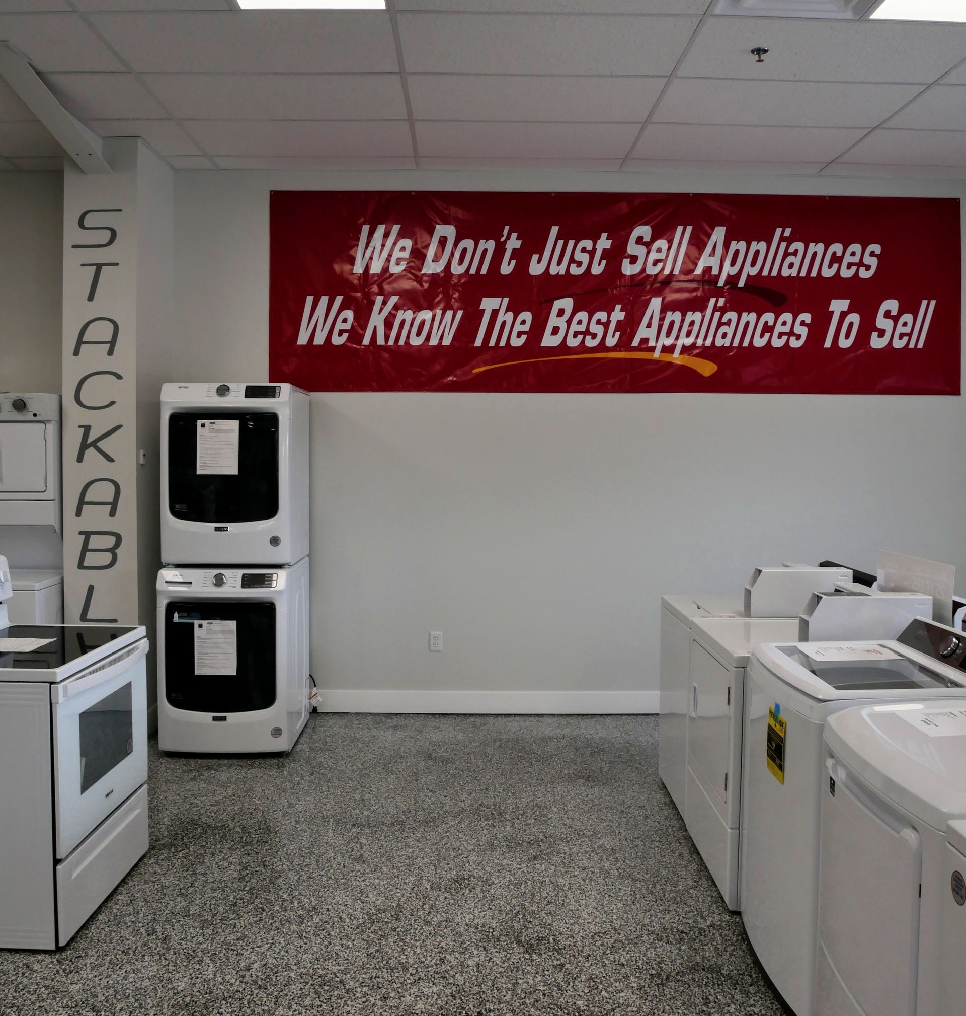 A showroom with appliances on display. A stacked washer and dryer are near a red banner reading 