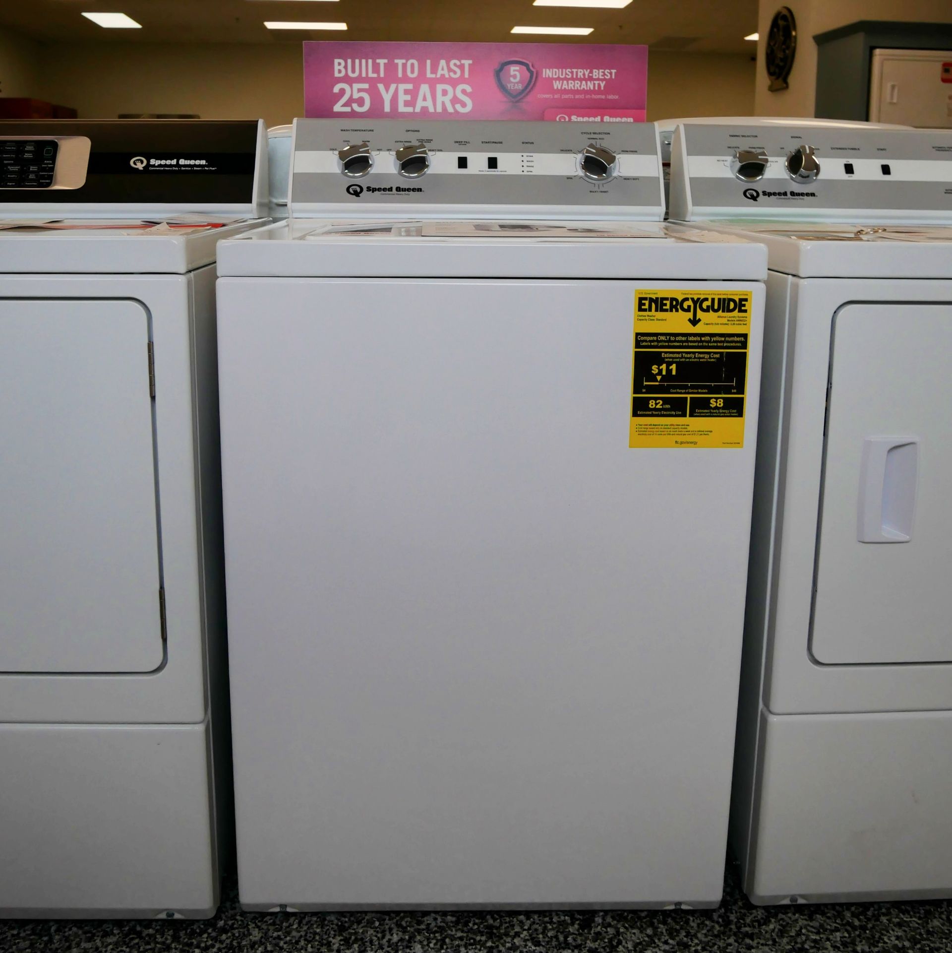 Row of white Speed Queen washing machines and dryers in a store, with an energy guide sticker on the middle one.