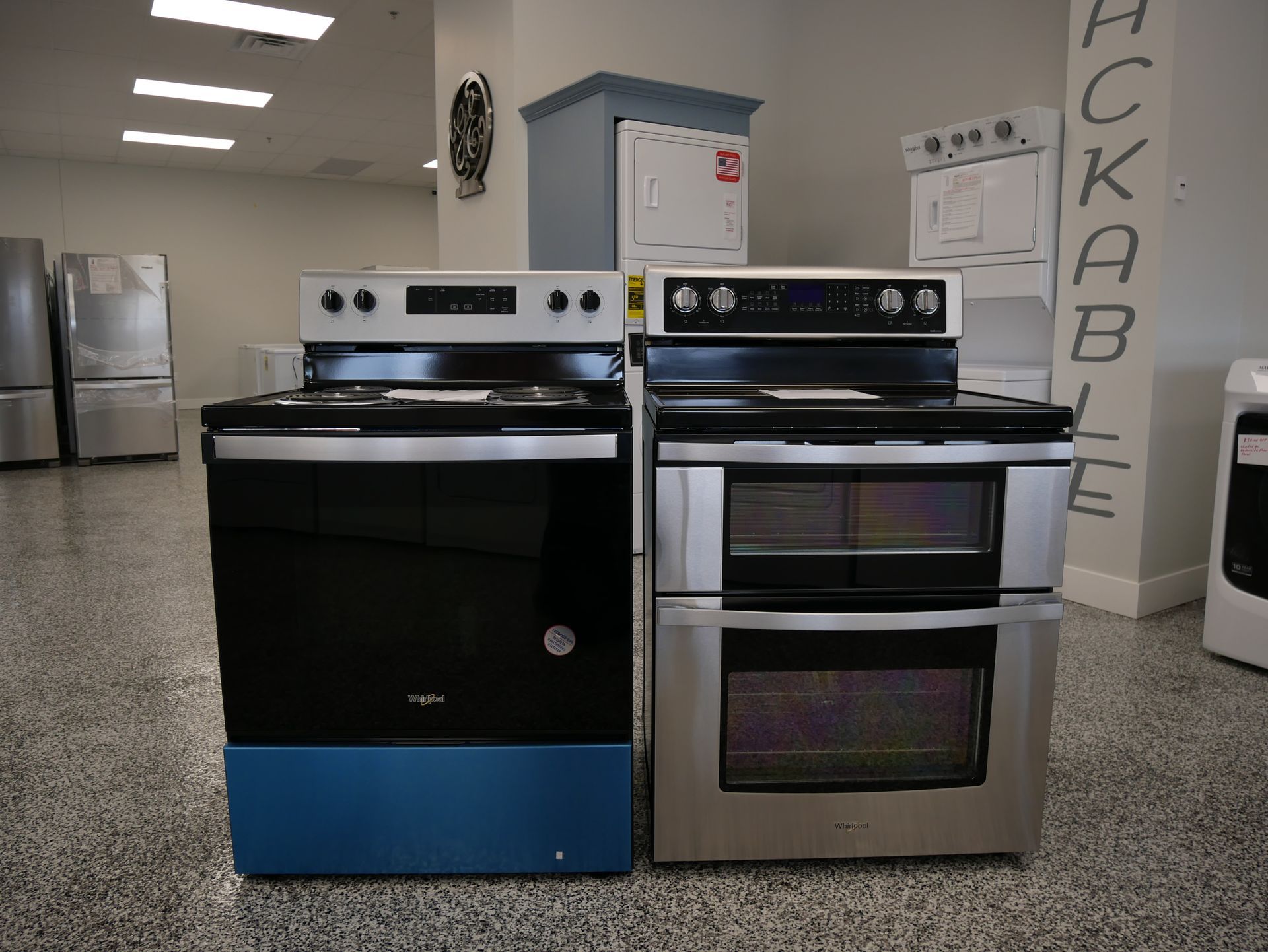 Two electric ranges: black and stainless steel. In a showroom setting.