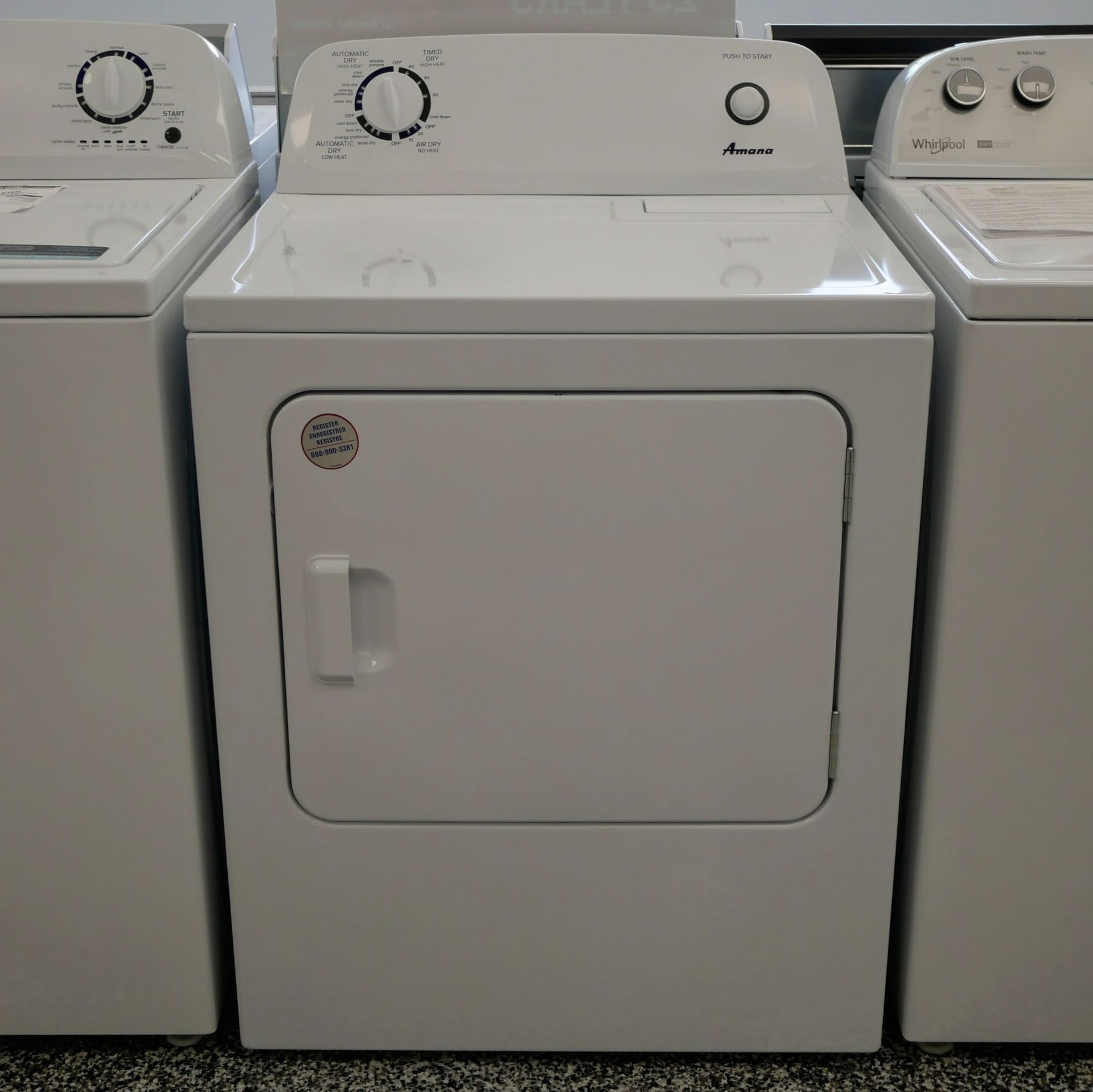White Amana dryer with control knobs, between a washer and another washer.