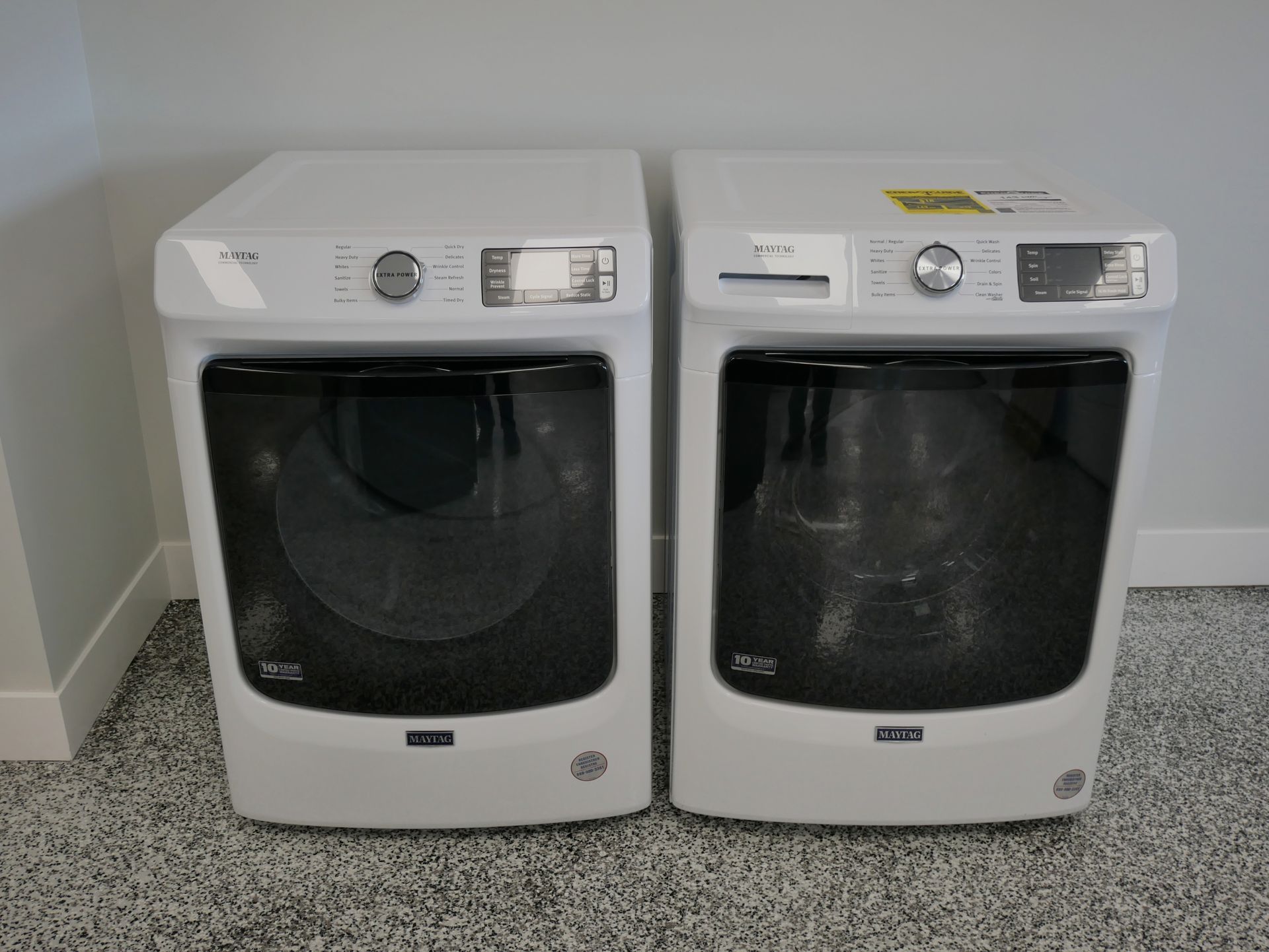 Two white washing machines with dark doors against a light gray wall.