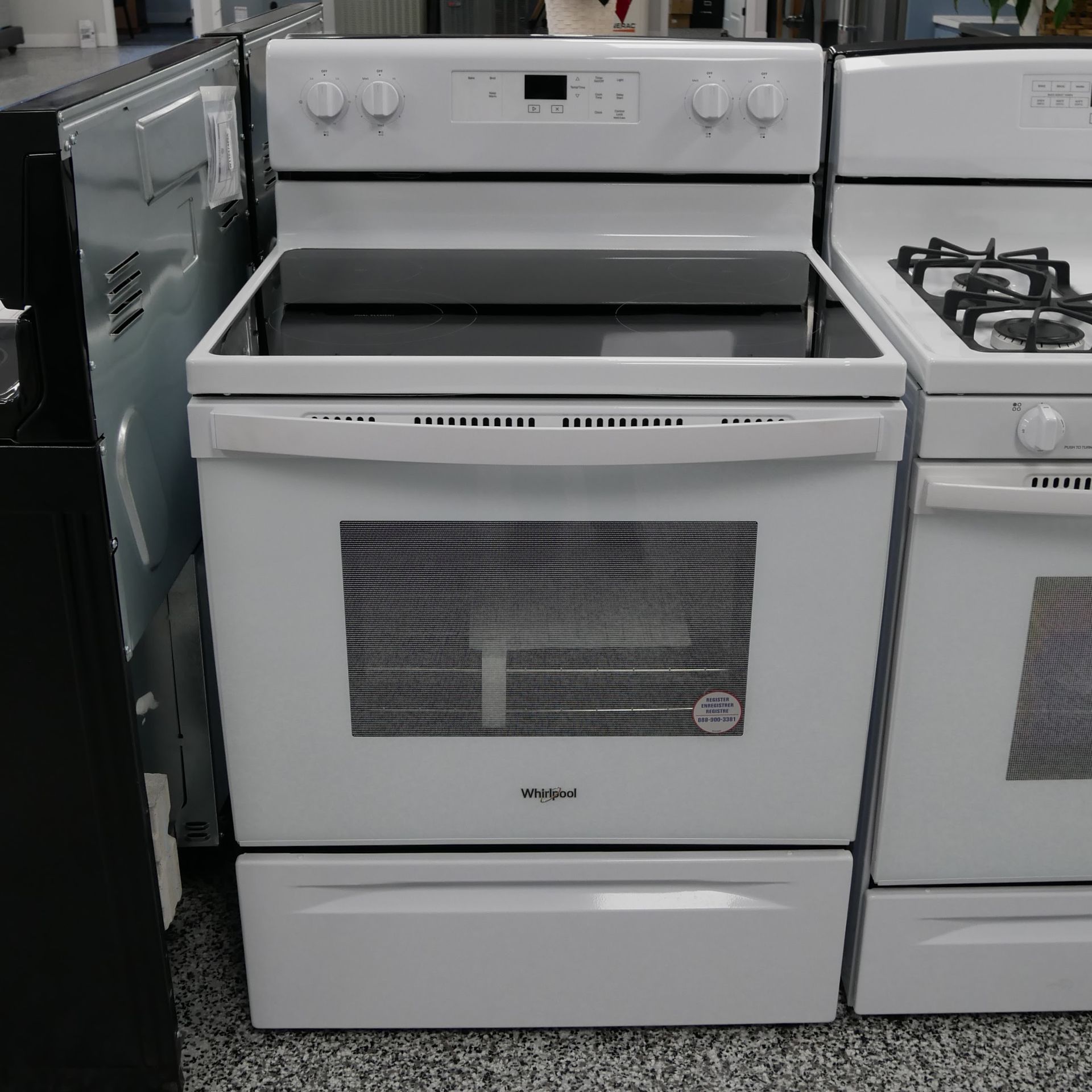 White Whirlpool electric range with glass cooktop and oven door, in appliance store.