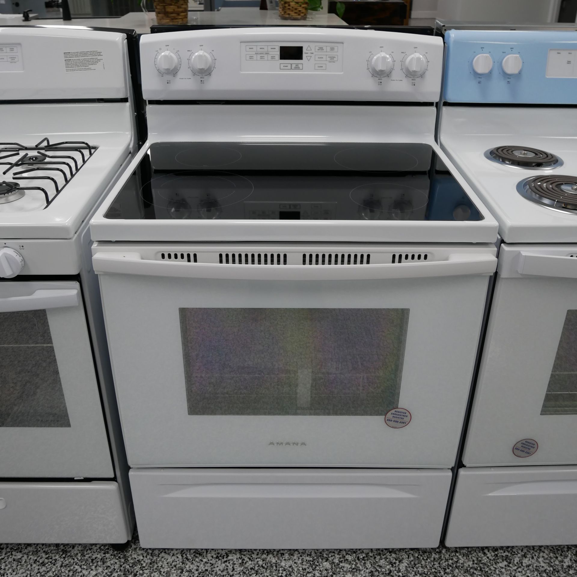 White electric range with black cooktop, in a row of other appliances in a showroom.